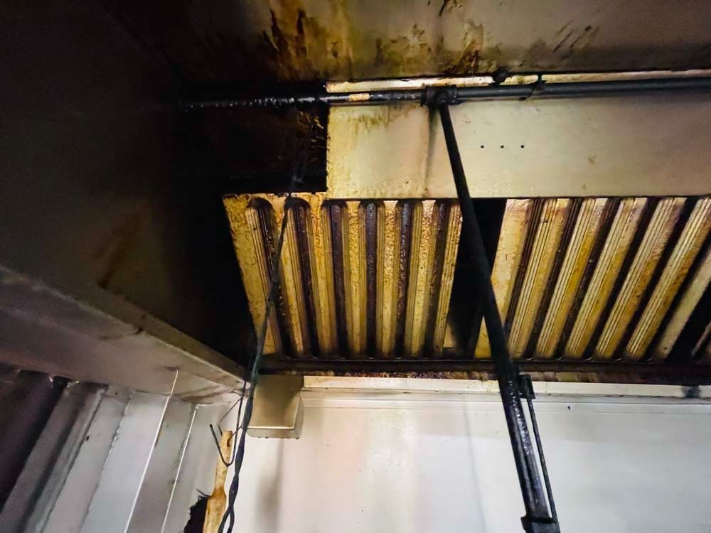 Greasy kitchen exhaust hood with stained metal, likely commercial.