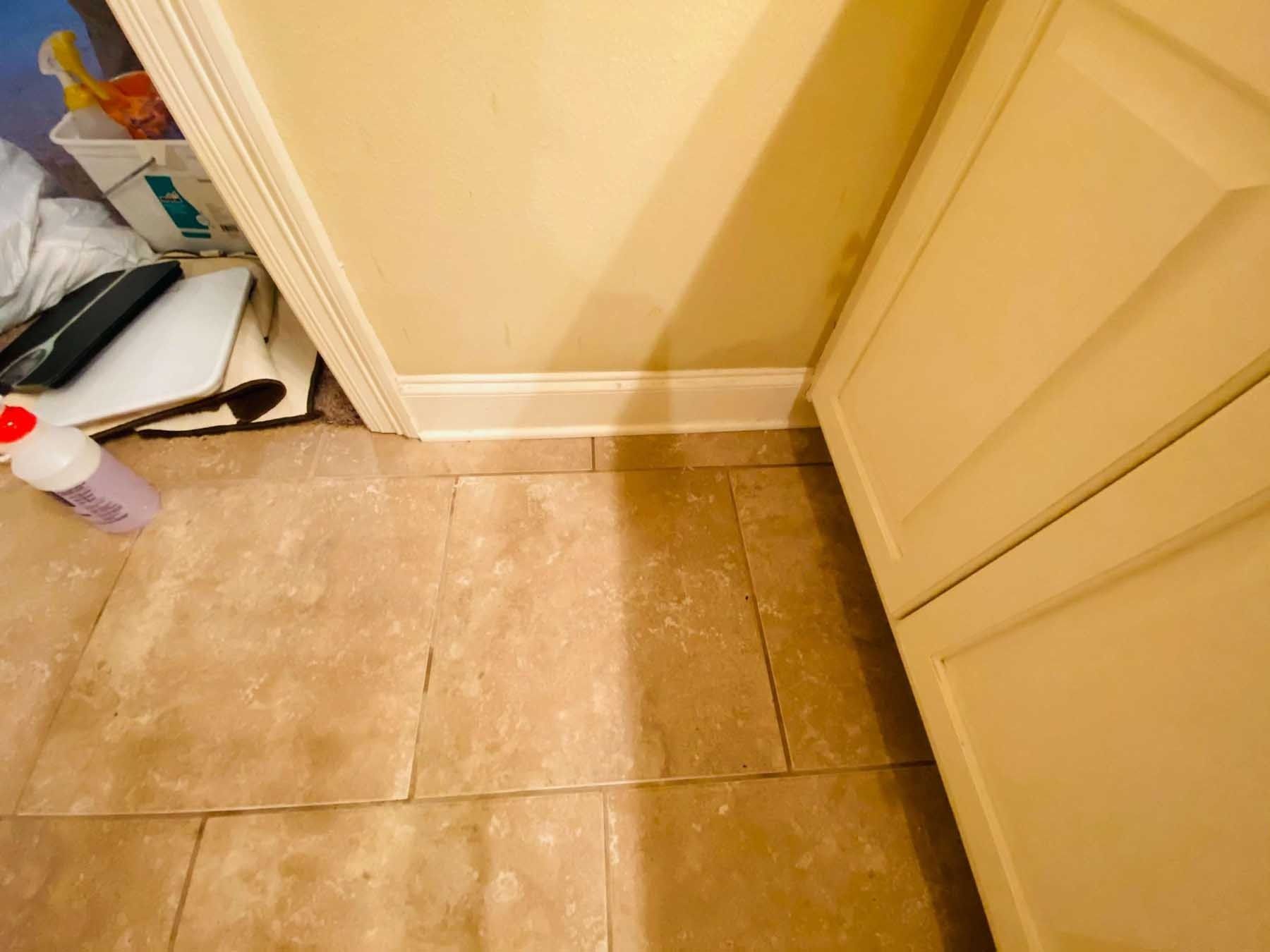 Tan tile floor with a white cabinet on the right and a wall with white molding on the left.