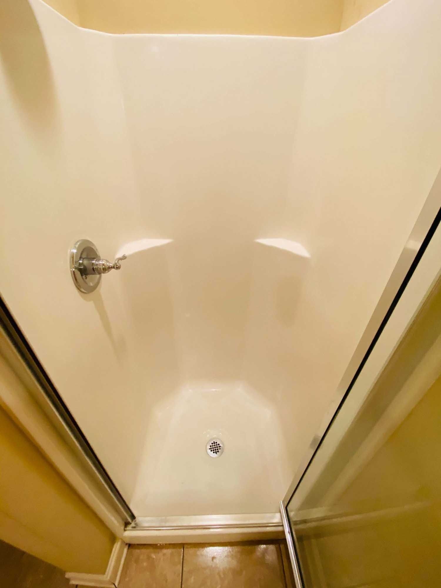 Interior view of a beige-colored shower with a sliding glass door and silver showerhead.