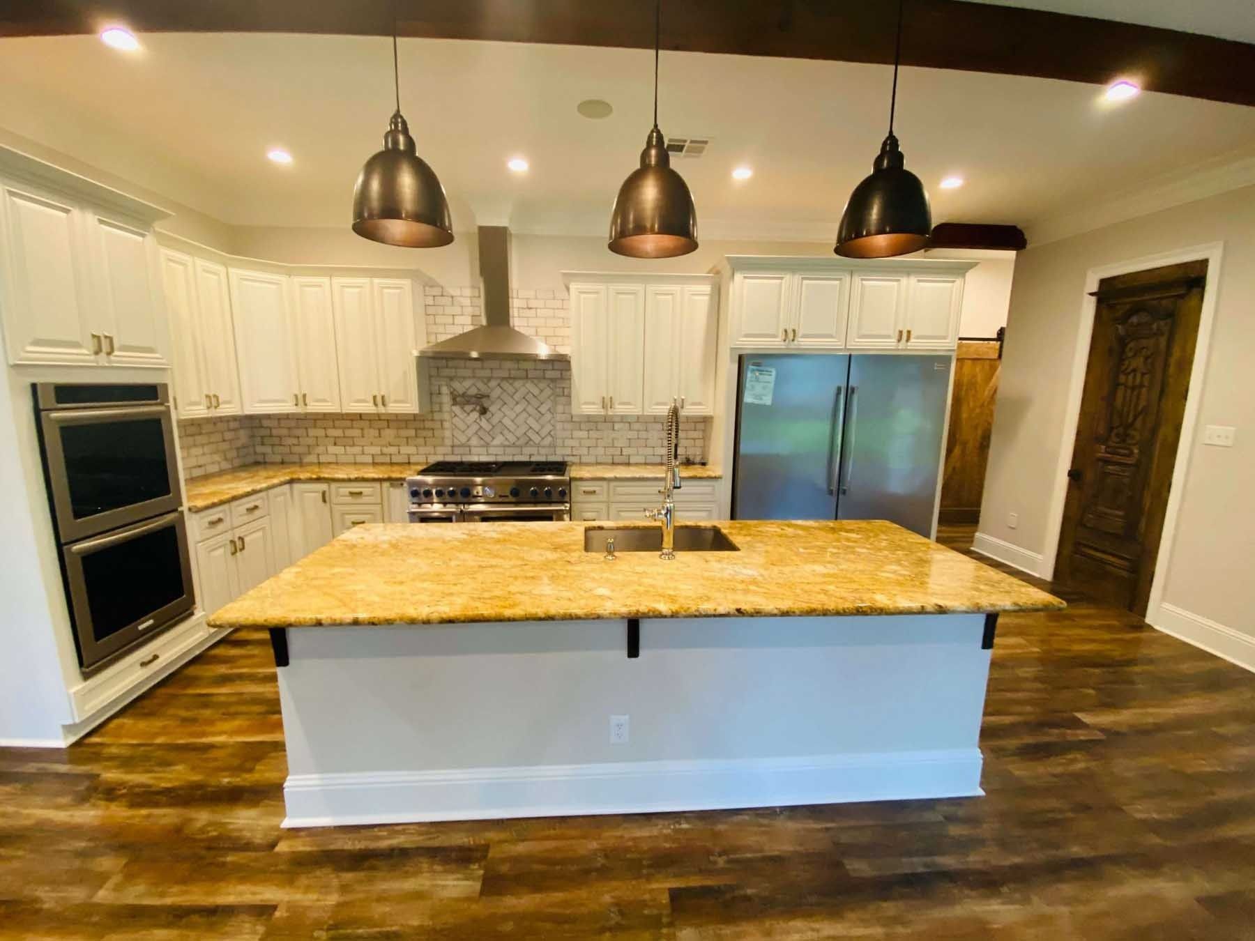 Kitchen with white cabinets, gold countertops, stainless steel appliances, and pendant lights.