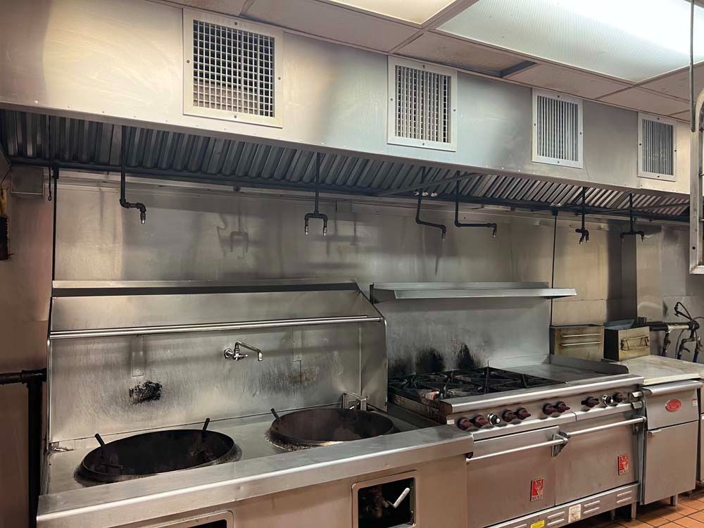 Commercial kitchen with stainless steel appliances, stove, vents.