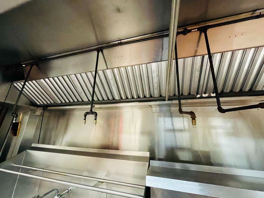 Stainless steel commercial kitchen hood with sprinkler system above sinks.