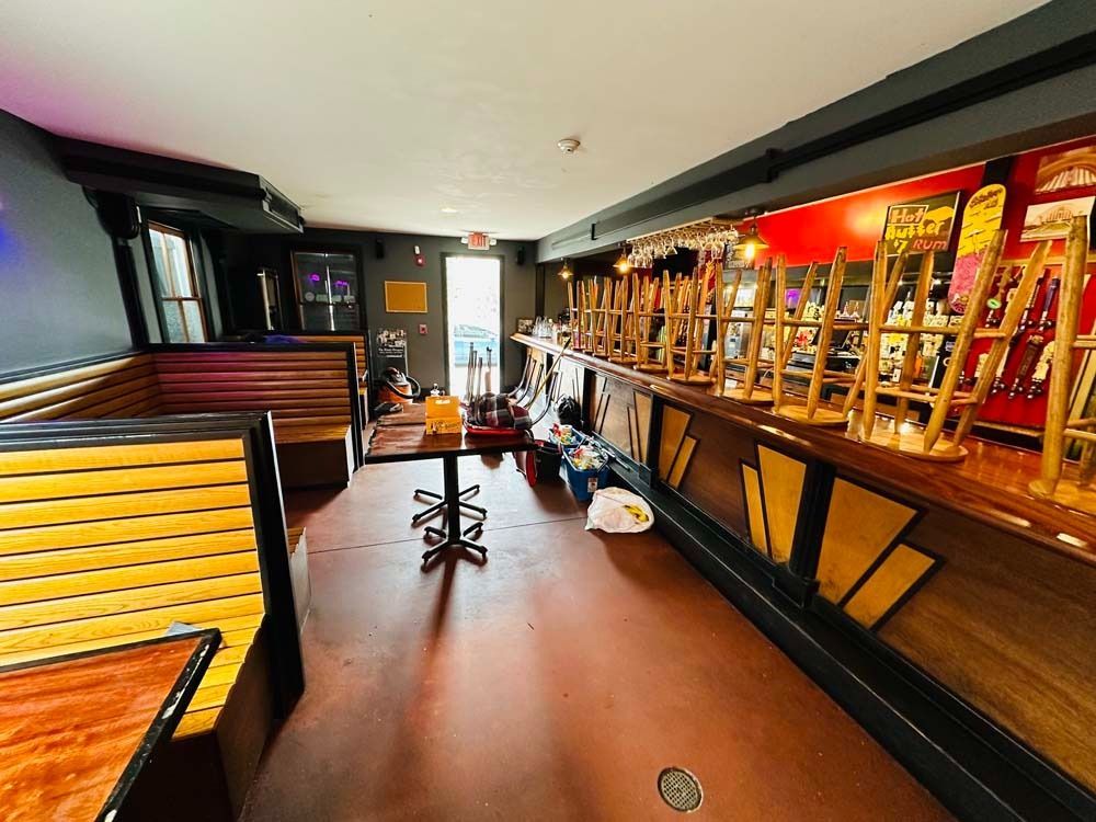 Empty bar interior with overturned stools, brown floor, red-lit back bar.