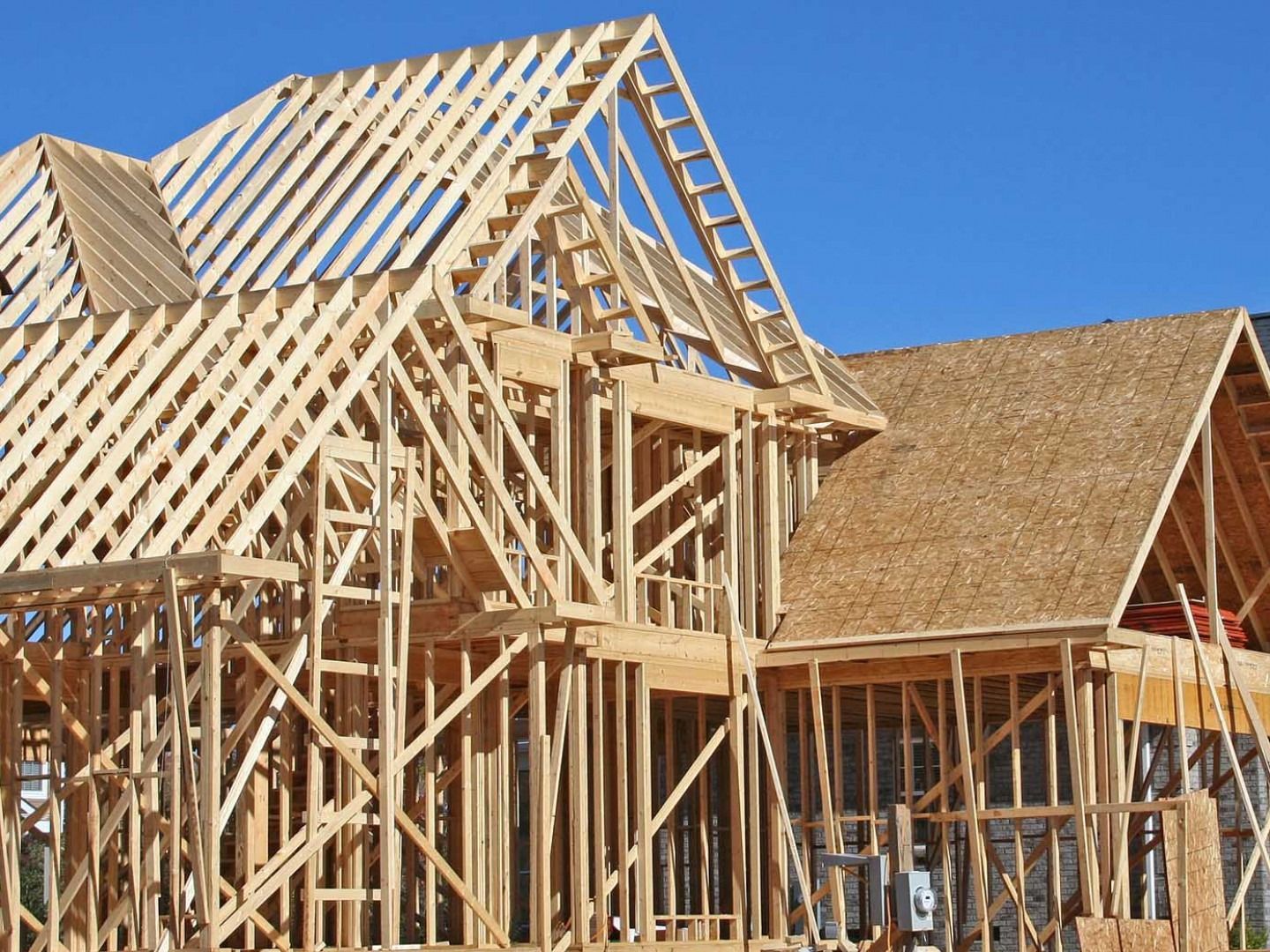 Wood frame of a house under construction against a blue sky.