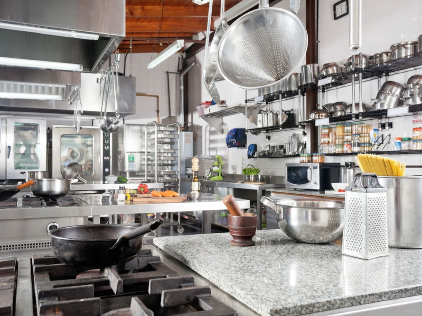 Commercial kitchen interior with stainless steel appliances, pots, pans, and a granite countertop.