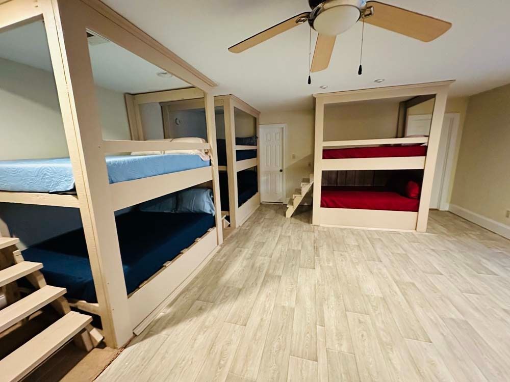 Bunk beds in a room with light wood-look flooring and a ceiling fan. Two beds have blue and red bedding.