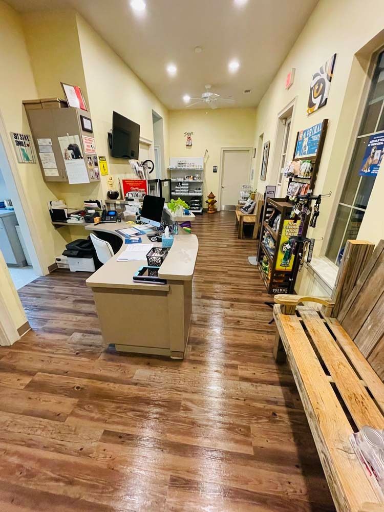 Reception area with desk, bench, displays, and doorway. Wooden floor and yellow walls.