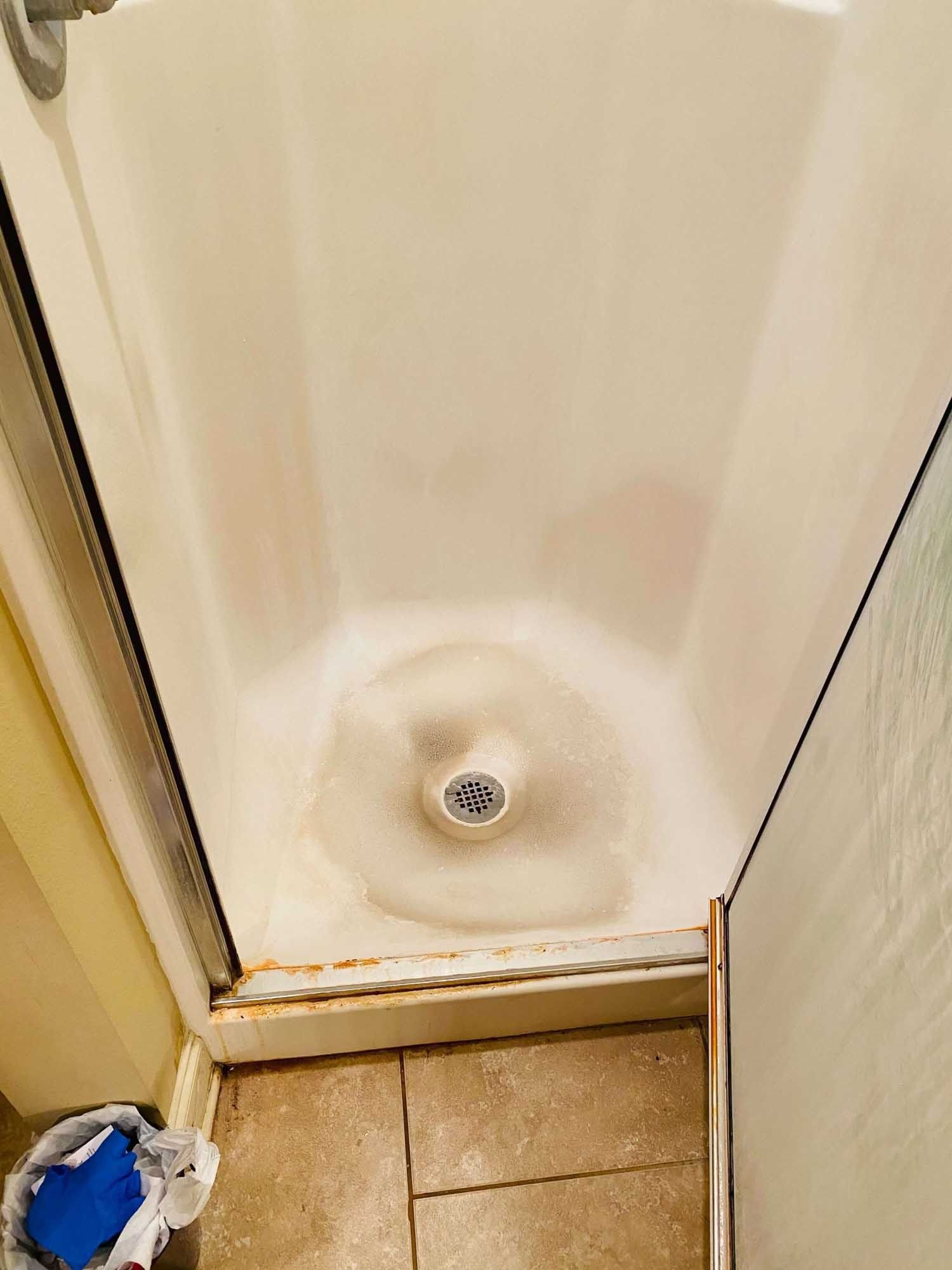 White shower stall with a drain, stains, and a partially open glass door.