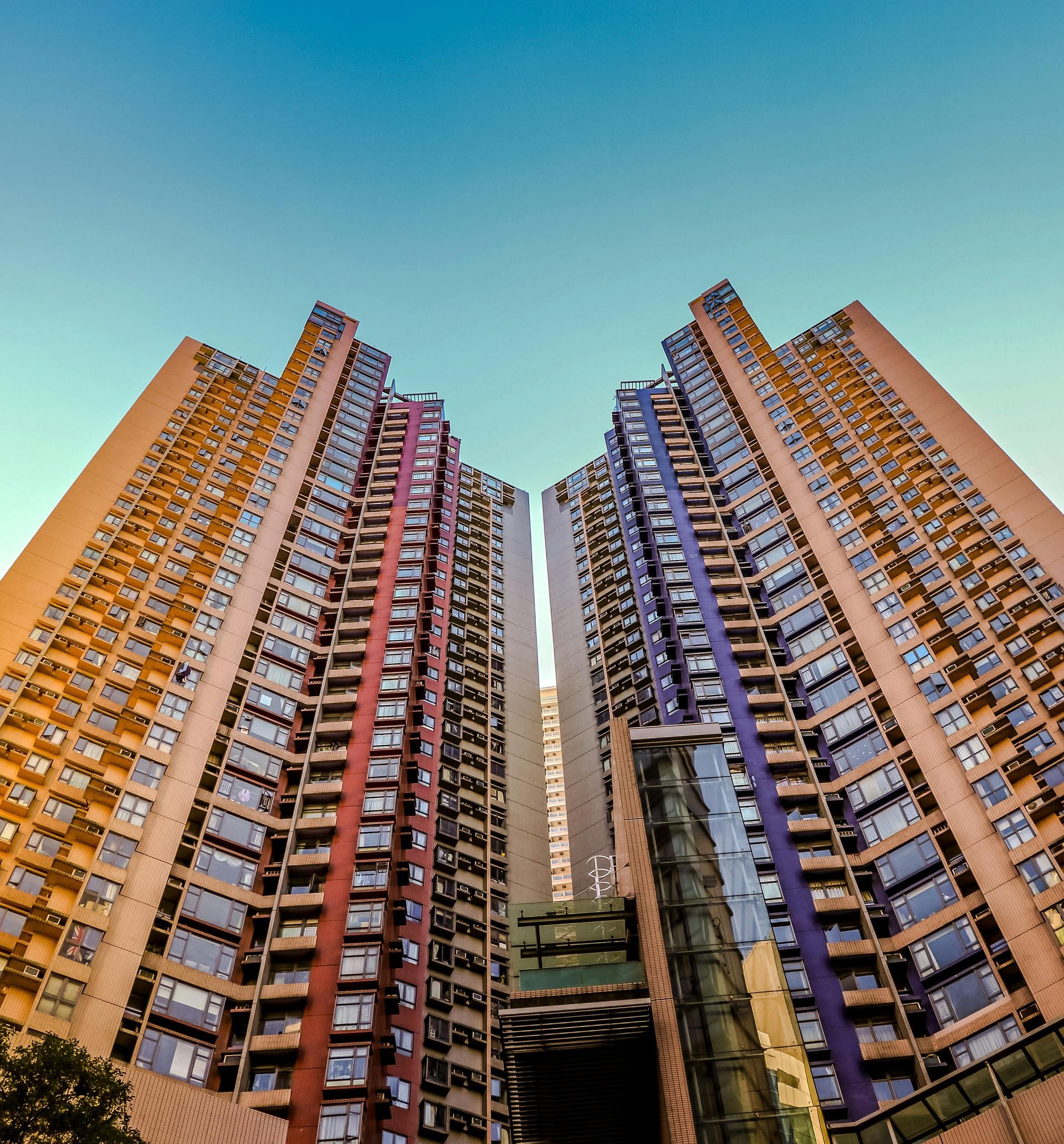 Two tall apartment buildings with colorful accents against a blue sky, viewed from a low angle.