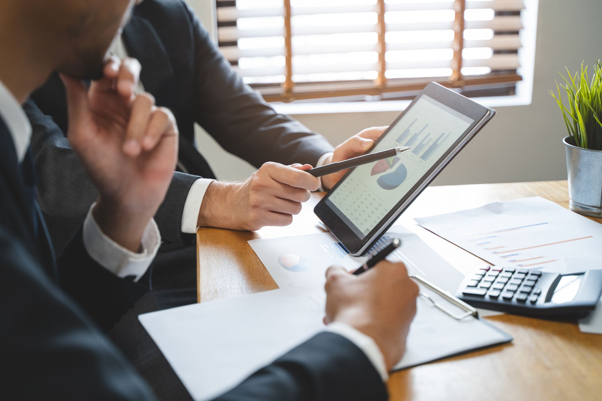 Two people in suits looking at financial charts on a tablet.