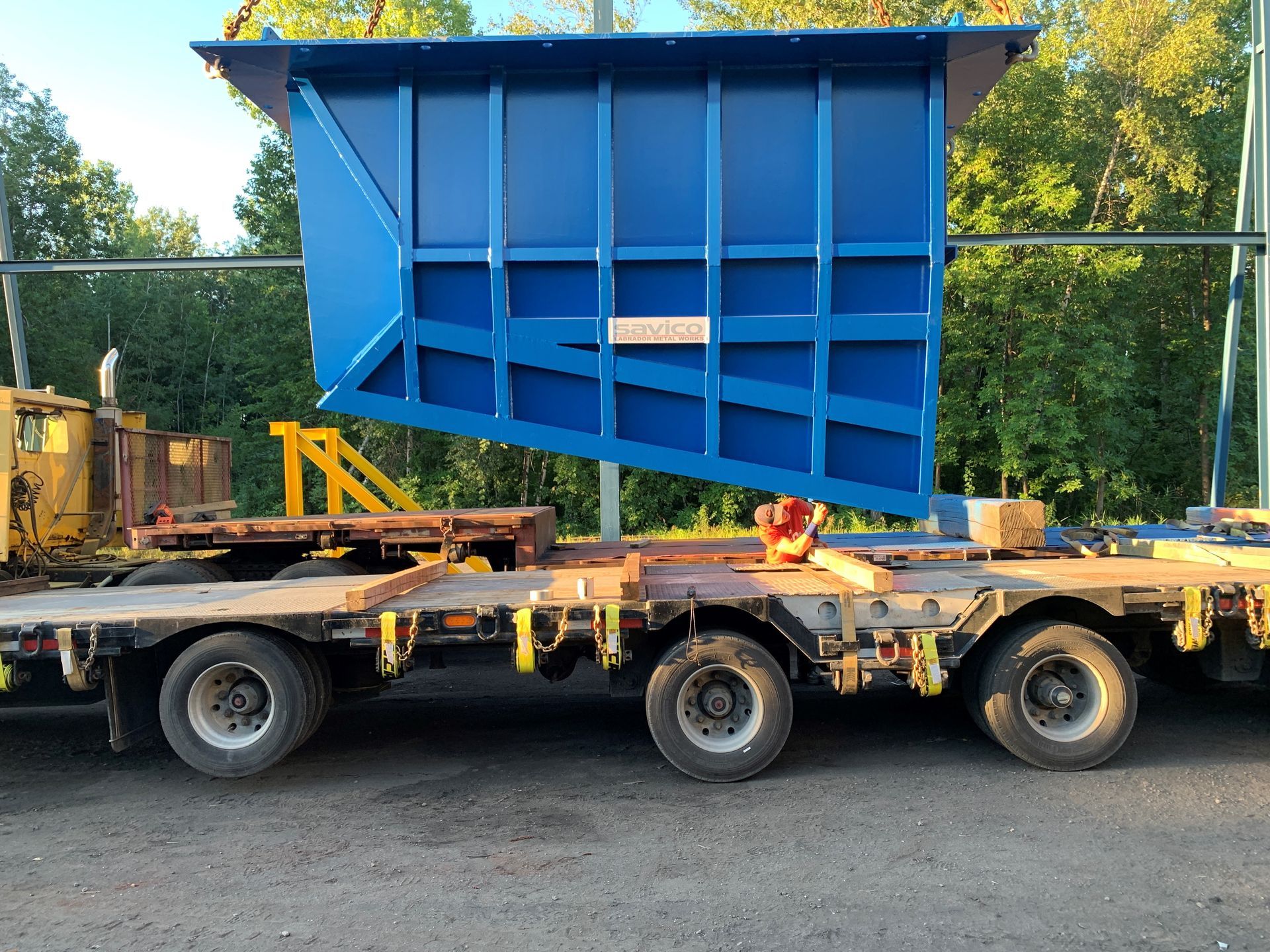 Conteneur industriel bleu chargé sur une remorque à plateau.