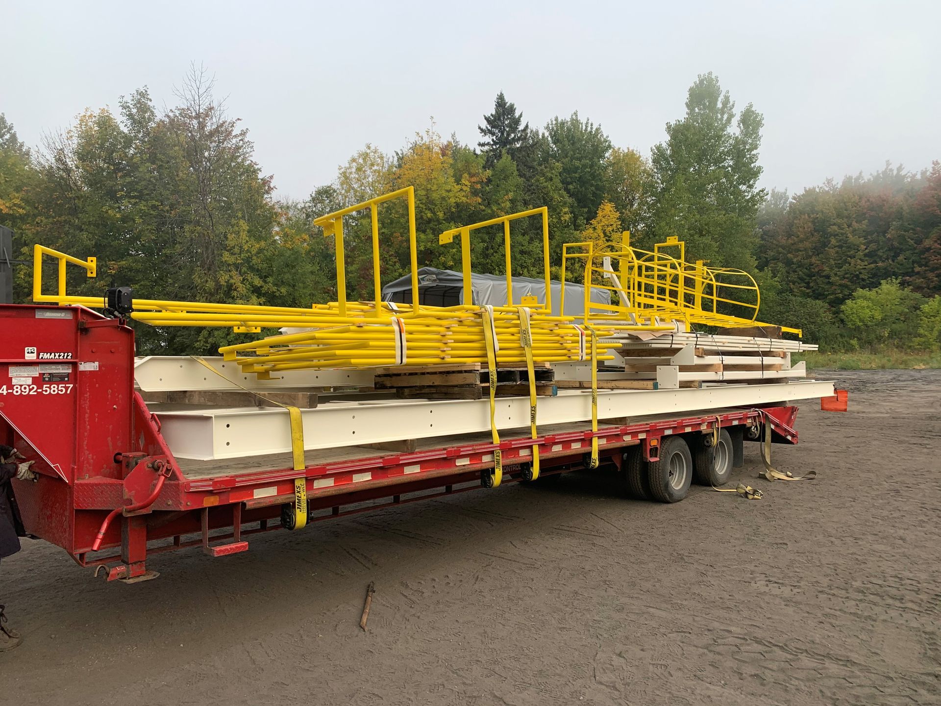 Des barrières de sécurité jaunes et des matériaux de construction chargés sur une remorque rouge dans un cadre extérieur.