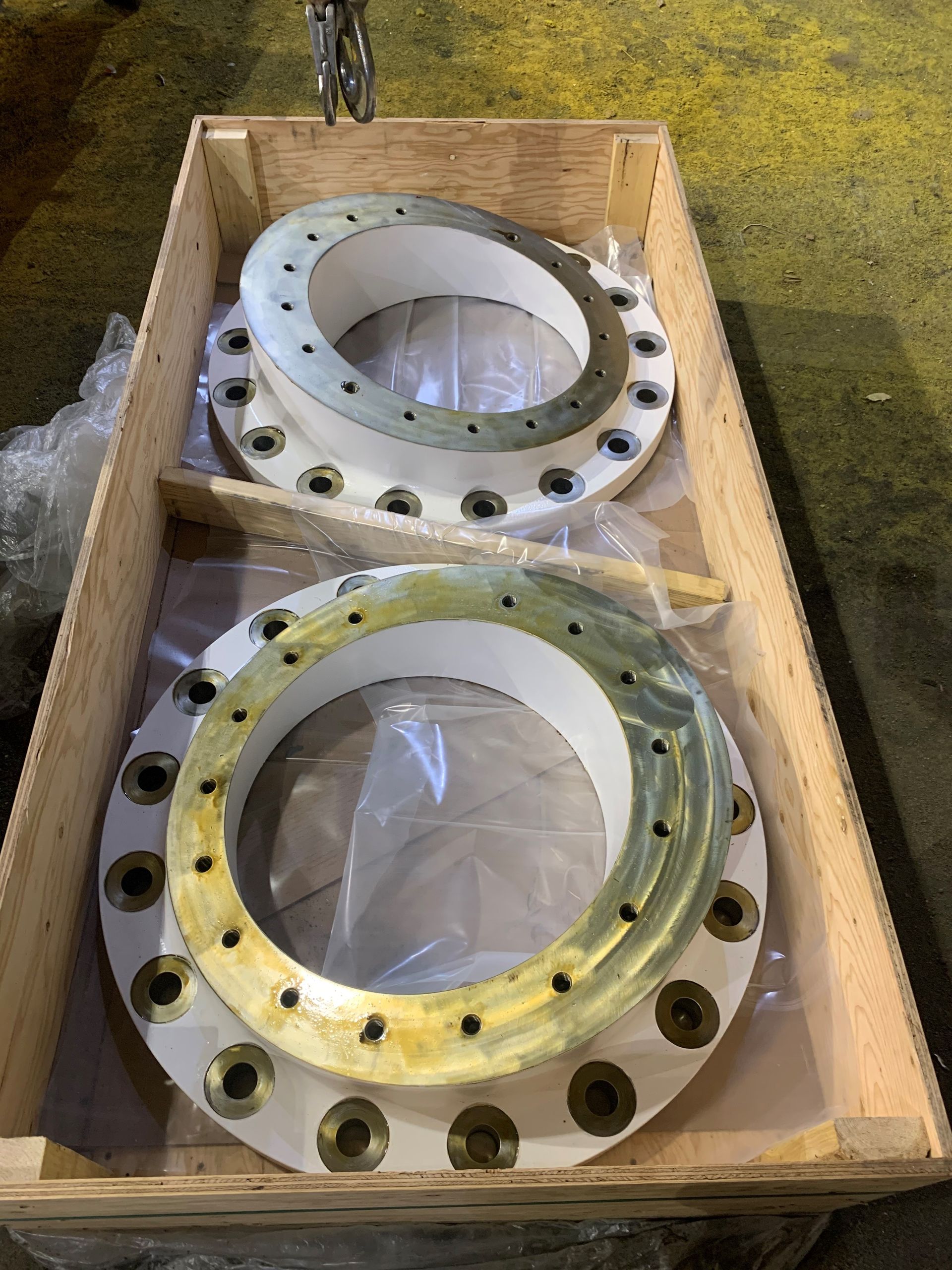 Deux grandes brides métalliques circulaires avec trous pour boulons, dans une caisse en bois.