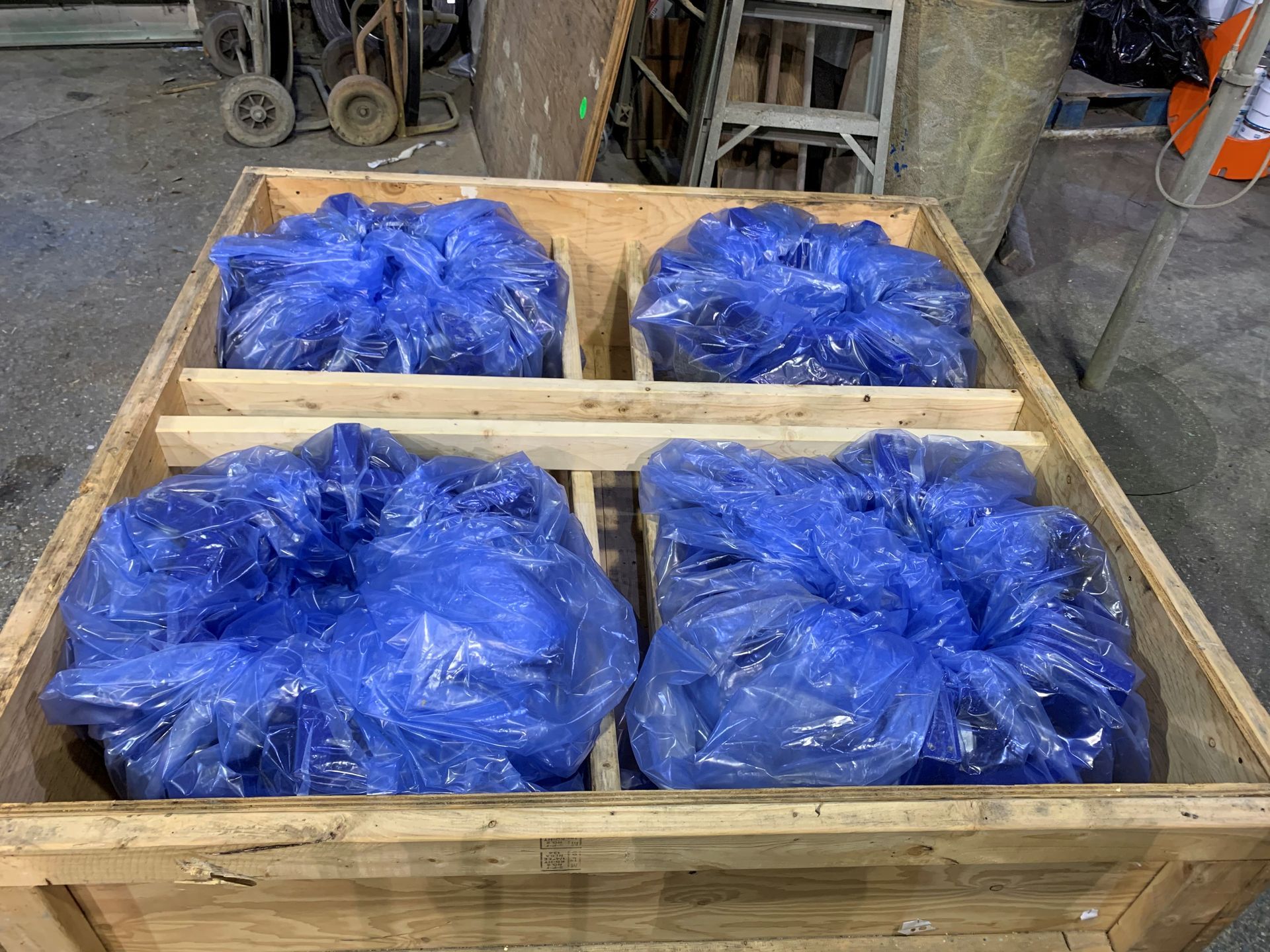 Une caisse en bois contenant quatre sections, chacune contenant un article emballé dans du plastique bleu.