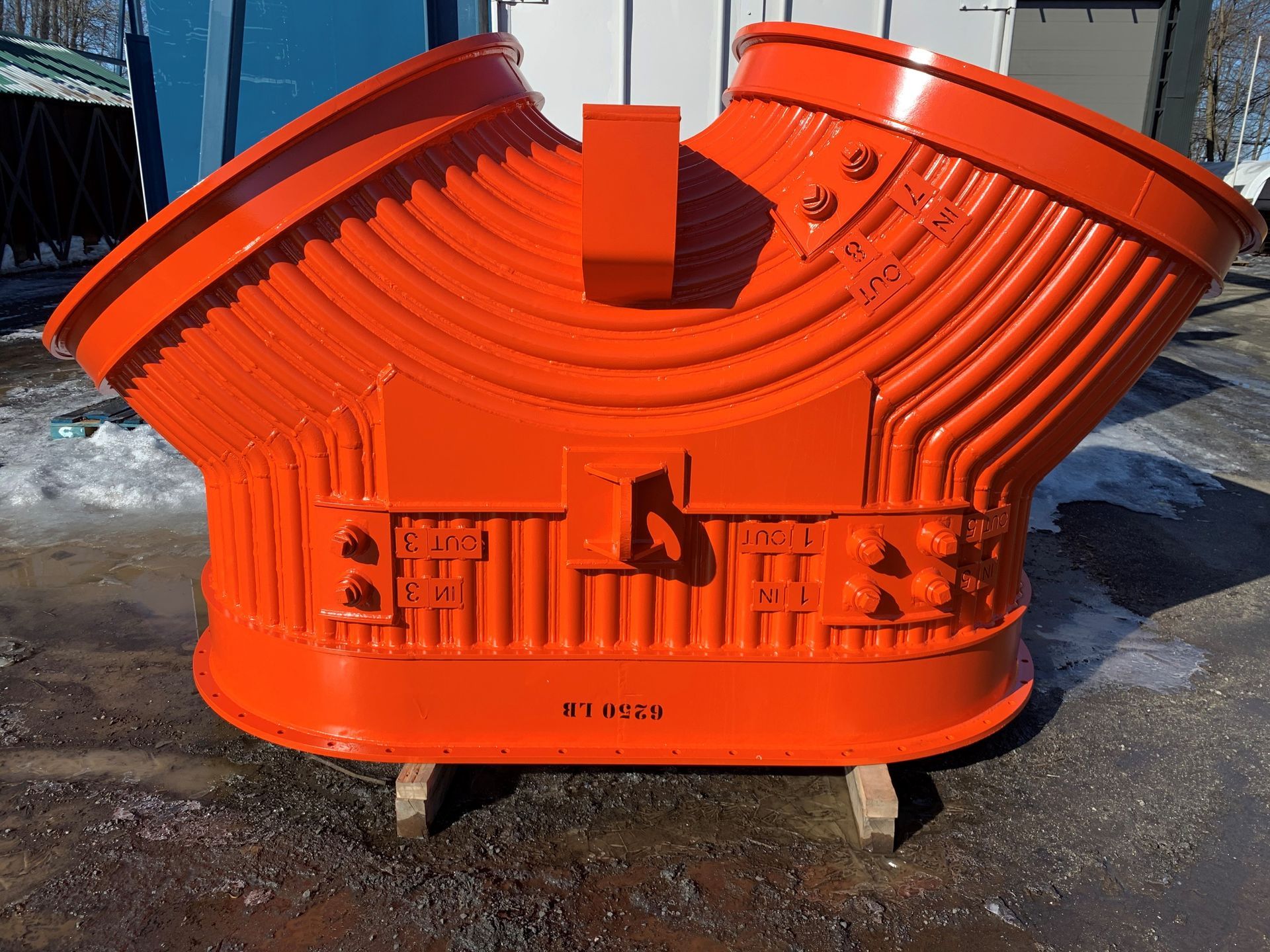 Composant industriel orange, ressemblant à un grand conduit, sur supports en bois à l'extérieur.