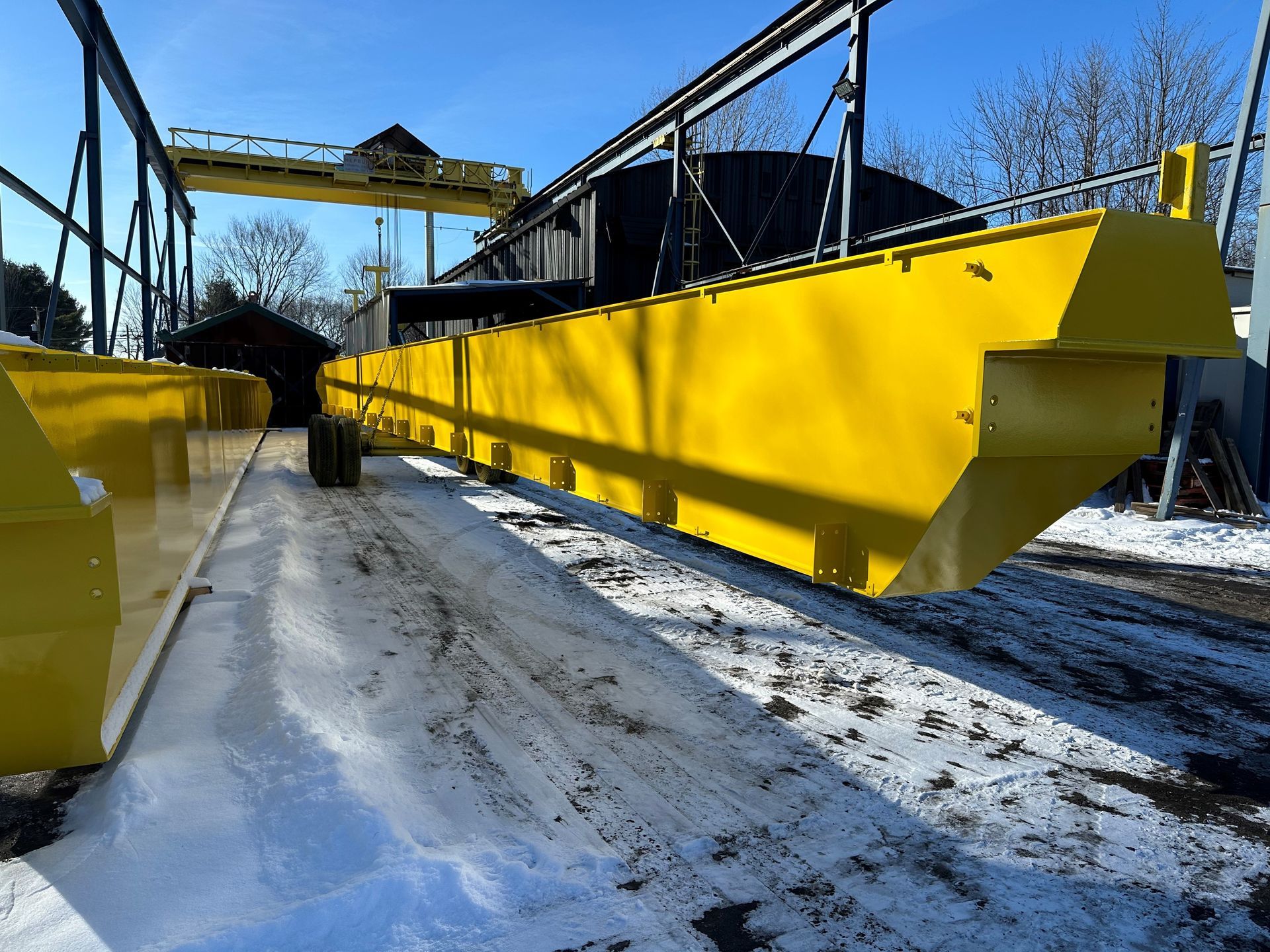 Poutre de pont roulant jaune dans un décor extérieur enneigé.