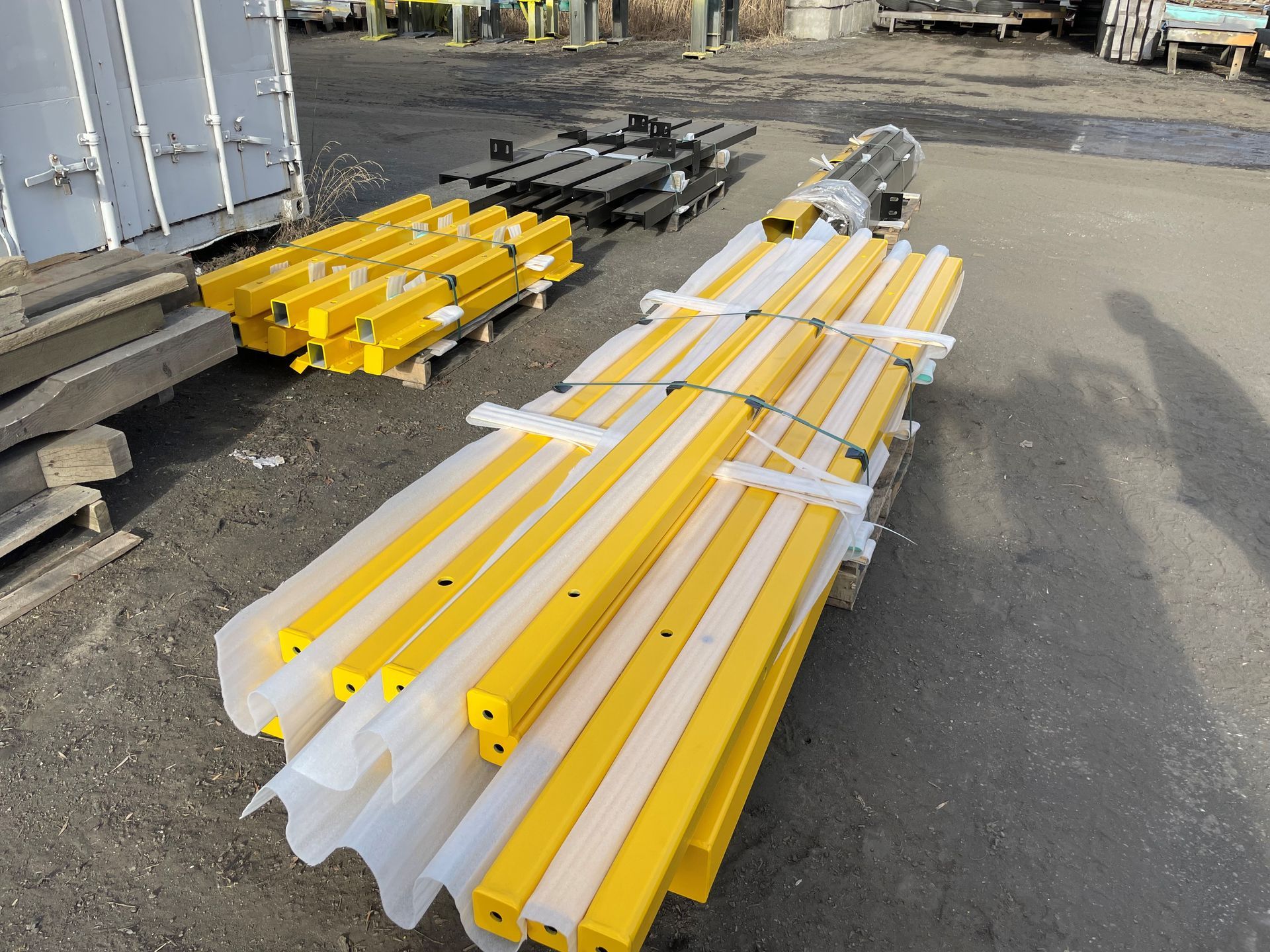 Des paquets de barres de métal jaune, certains empilés, à l'extérieur sur le trottoir.