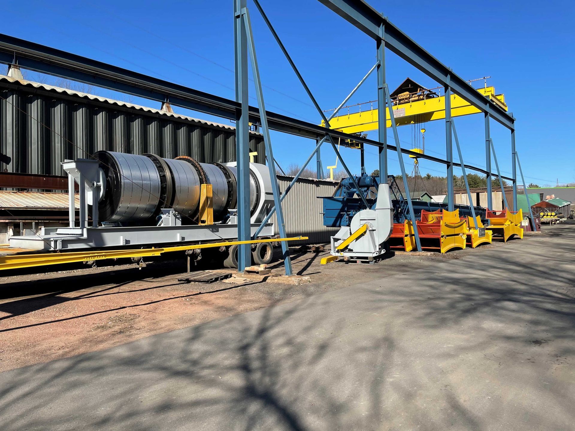 Gros équipement industriel sur une remorque, sous une grue, dans une cour.
