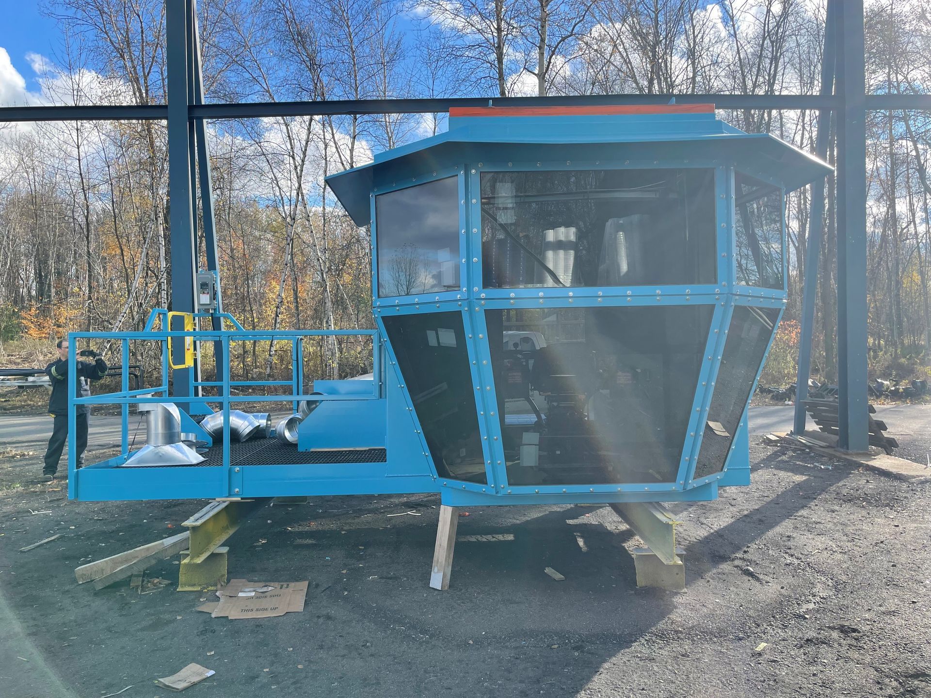 Cabine industrielle bleue avec vitres grillagées, à l'extérieur devant une forêt.