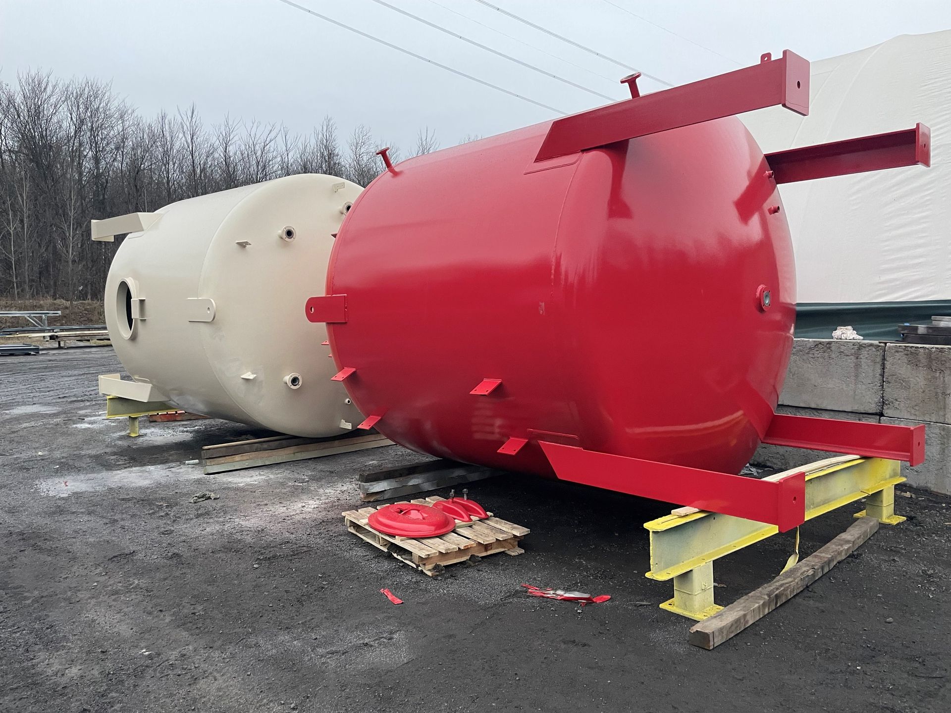 Réservoirs cylindriques rouges et beiges en extérieur. Le réservoir rouge repose sur un support jaune ; le réservoir beige est posé à côté.