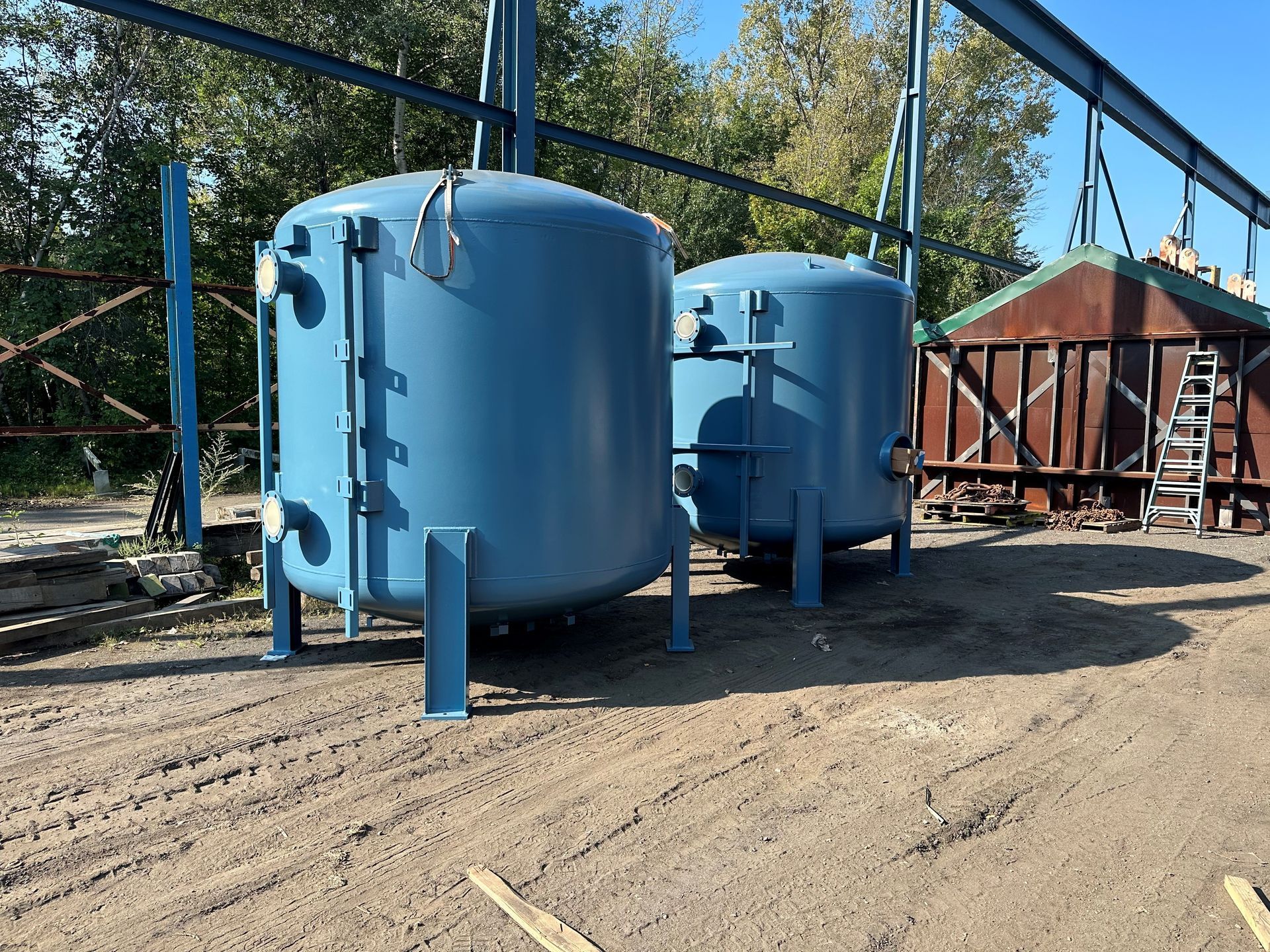 Deux réservoirs industriels bleus posés sur des supports métalliques à l'extérieur, près d'une structure rouillée.
