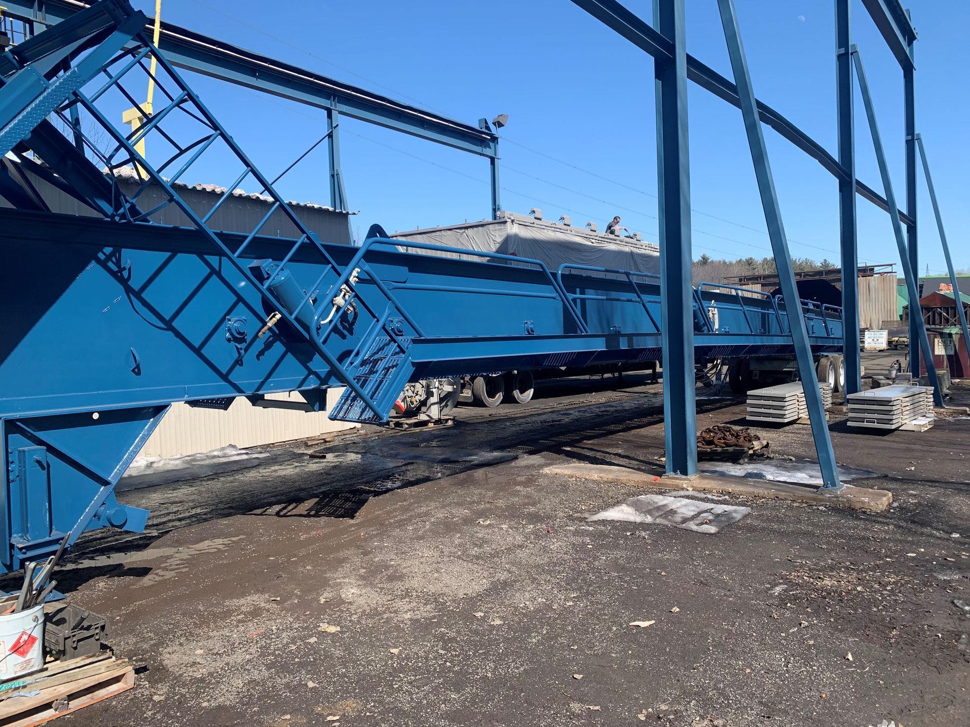 Remorque industrielle bleue sous châssis de construction, chargée de matériaux sur sol asphalté.