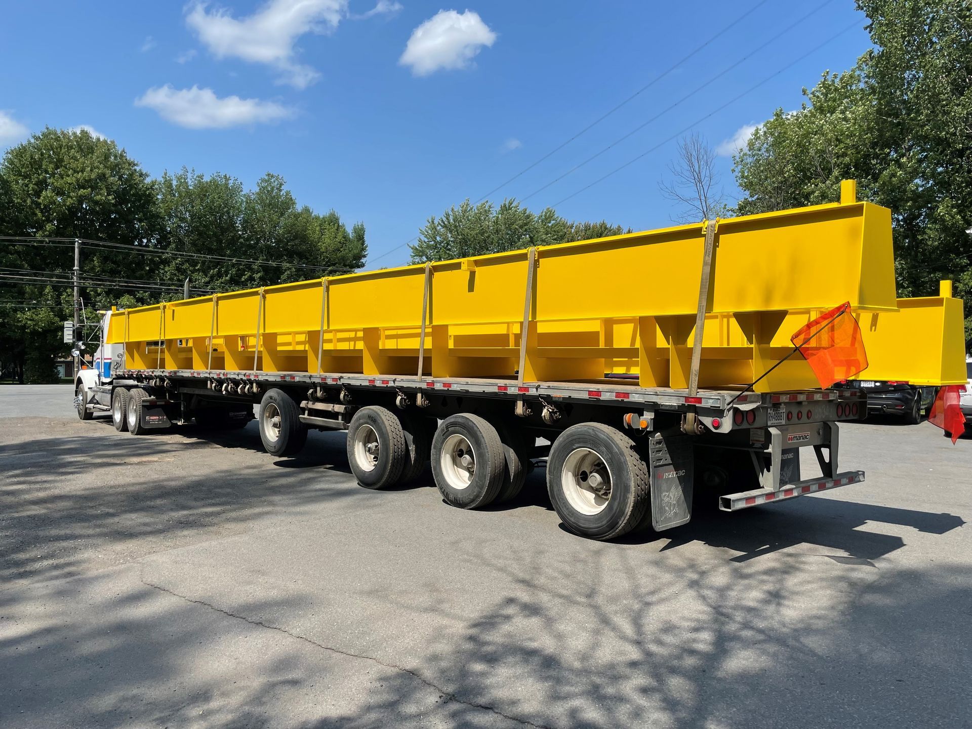 Structure métallique jaune sur un camion à plateau, sous un ciel bleu avec des arbres en arrière-plan.