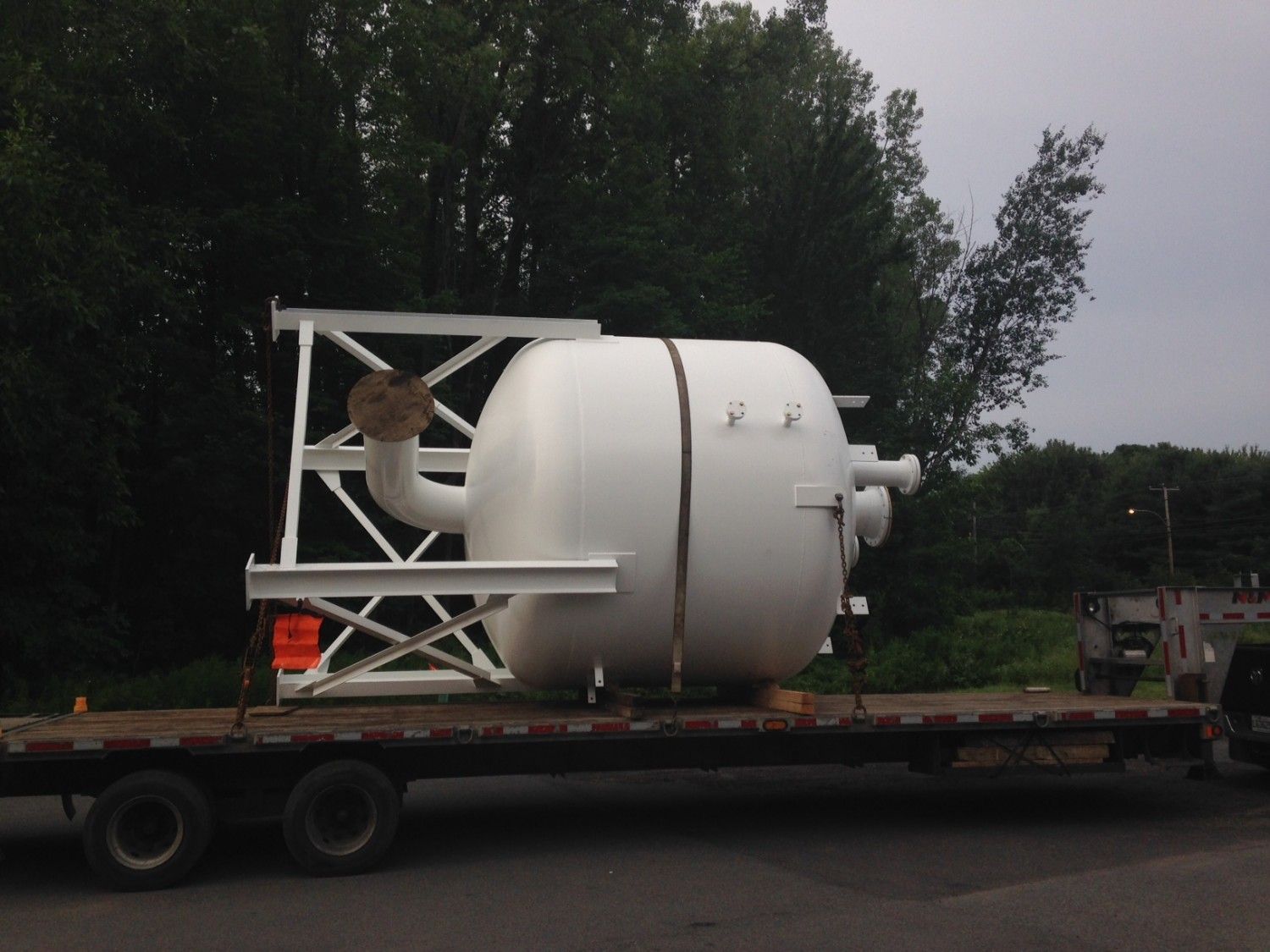 Citerne industrielle blanche sur une remorque à plateau, soutenue par un cadre en acier, à l'extérieur.