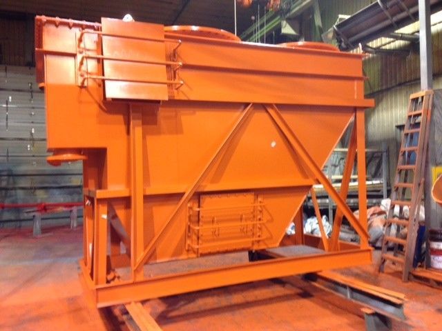 Trémie industrielle orange en configuration d'usine, soutenue par un cadre métallique.