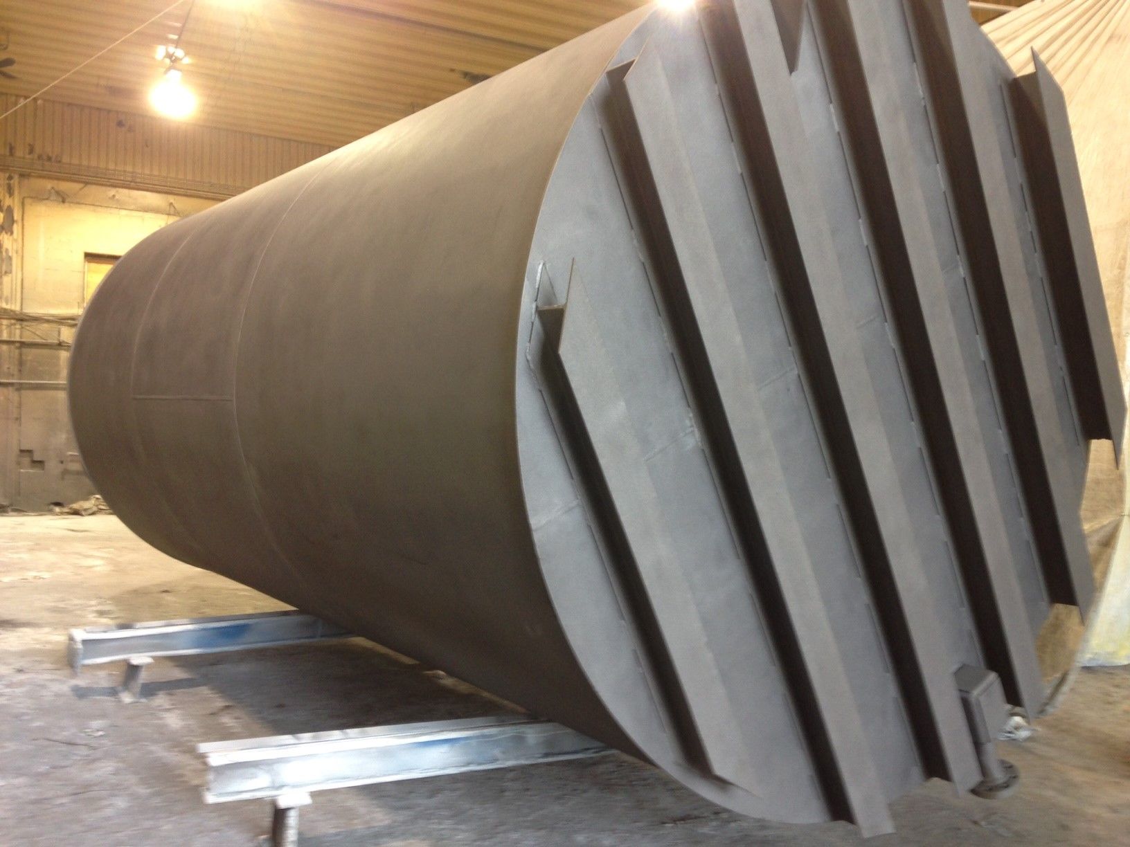 Grand réservoir industriel cylindrique foncé, avec des ailettes inclinées à une extrémité, soutenu par des poutres métalliques.