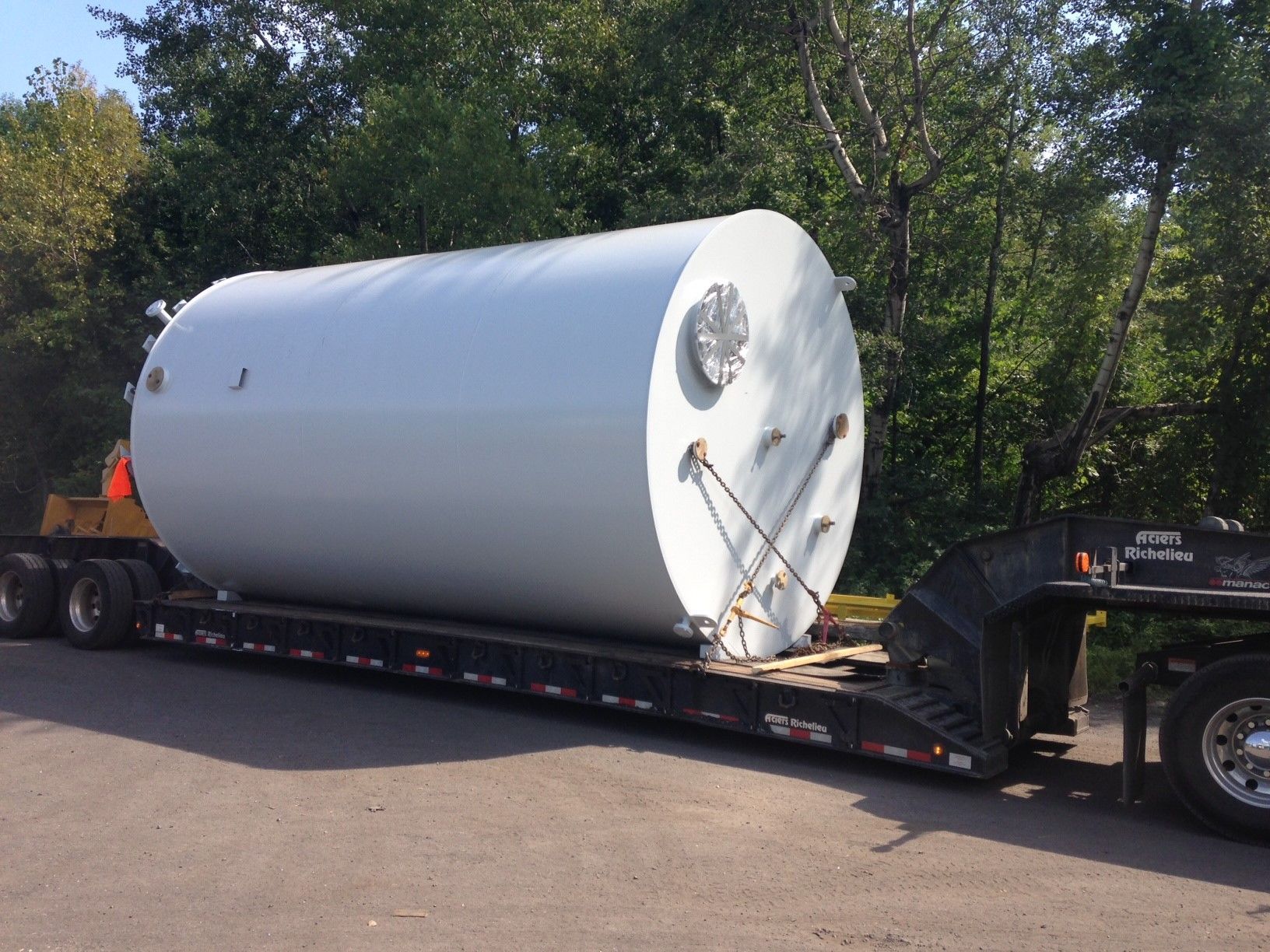 Grand réservoir cylindrique blanc fixé sur une remorque à plateau, prêt à être transporté à l'extérieur.