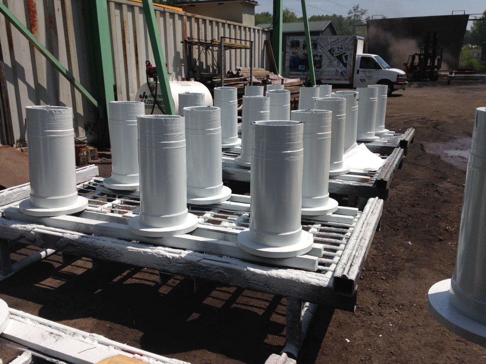 Objets métalliques cylindriques blancs, recouverts de peinture, disposés sur des étagères à l'extérieur.