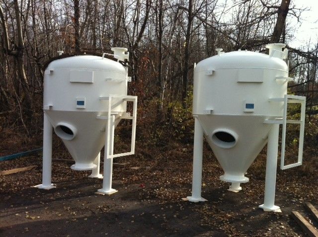 Deux silos industriels blancs à fonds coniques, dans un cadre extérieur boisé.