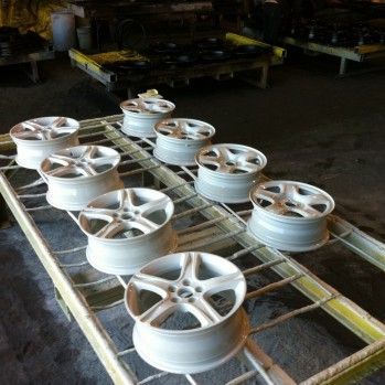 Jantes de voiture blanches disposées sur un support en métal jaune dans un décor industriel.