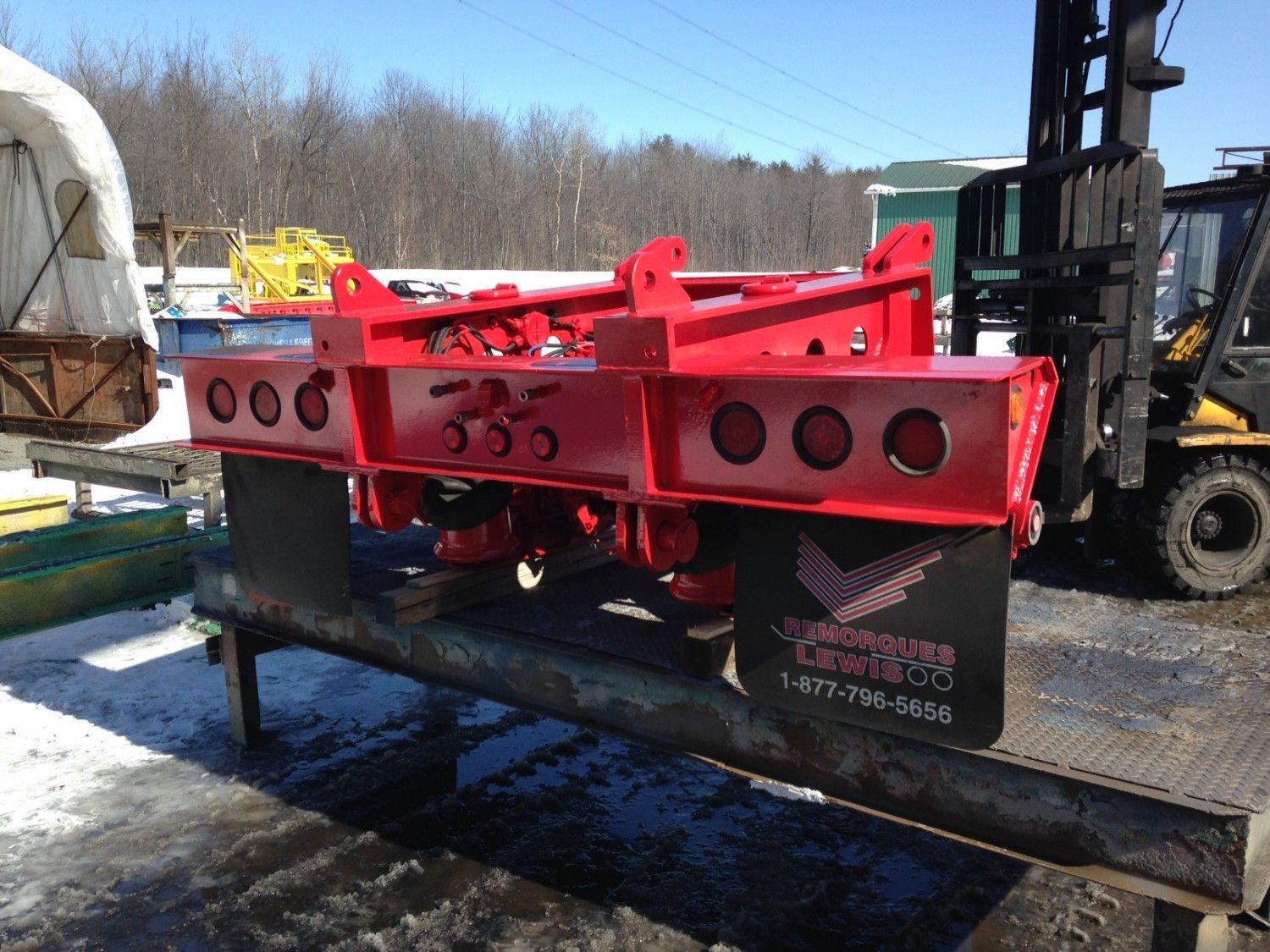 Machine industrielle rouge sur un support métallique, près d'un chariot élévateur. La machine présente plusieurs découpes circulaires.