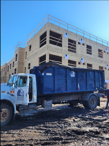 A blue roll-off dumpster is positioned beside an active cleanup area.