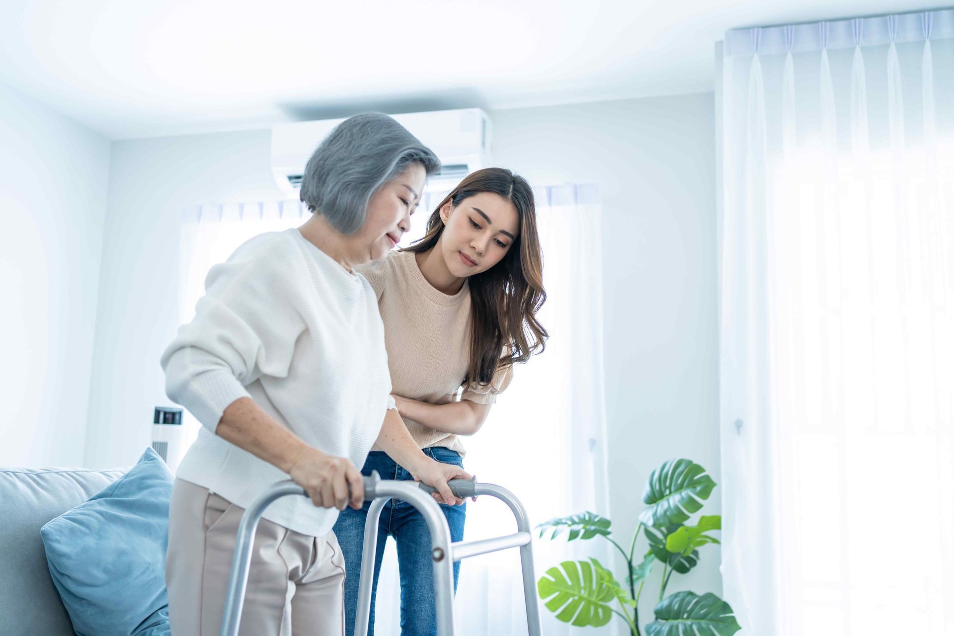 A young woman is helping an older woman use a walker.