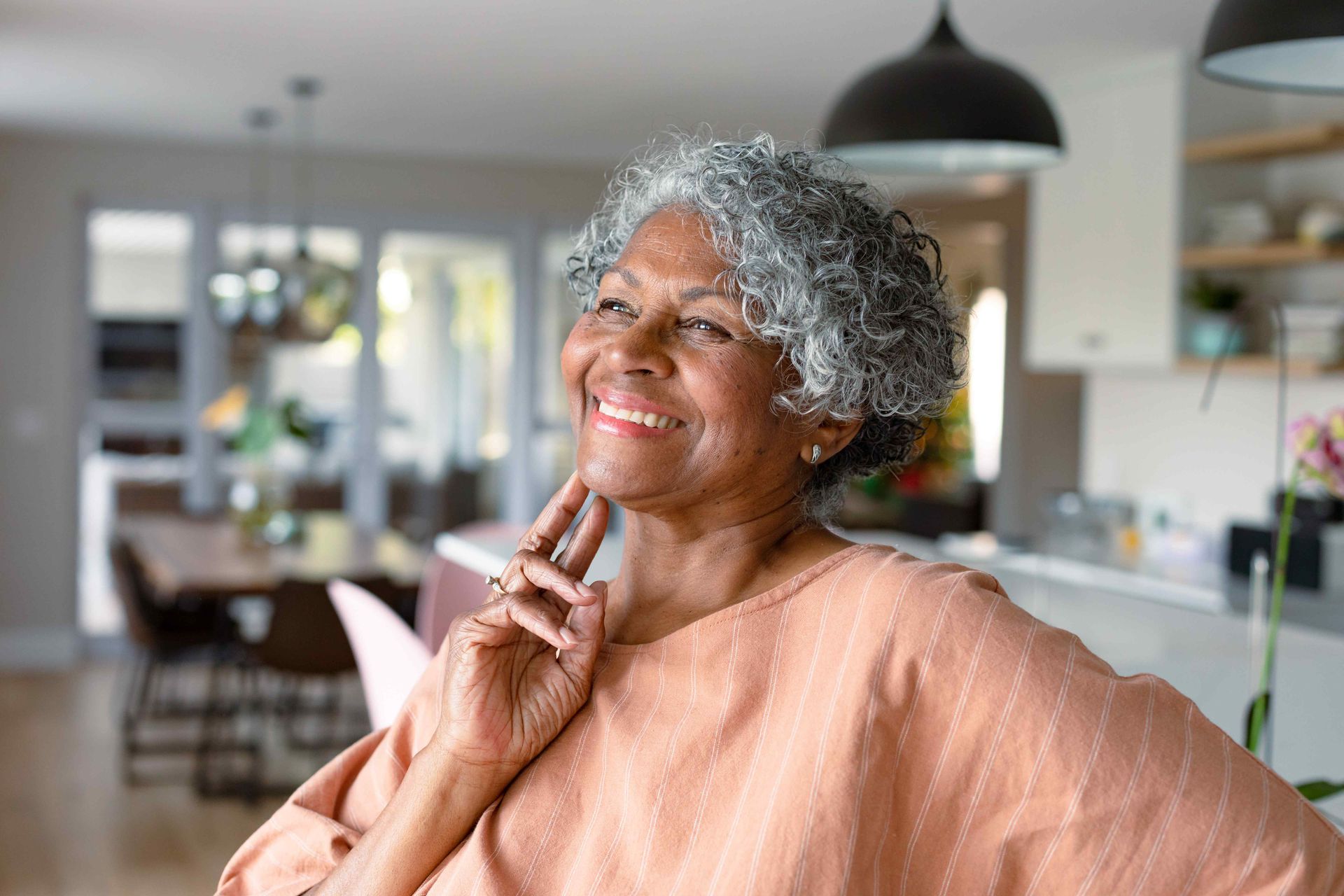 An older woman with gray hair is smiling in a living room.
