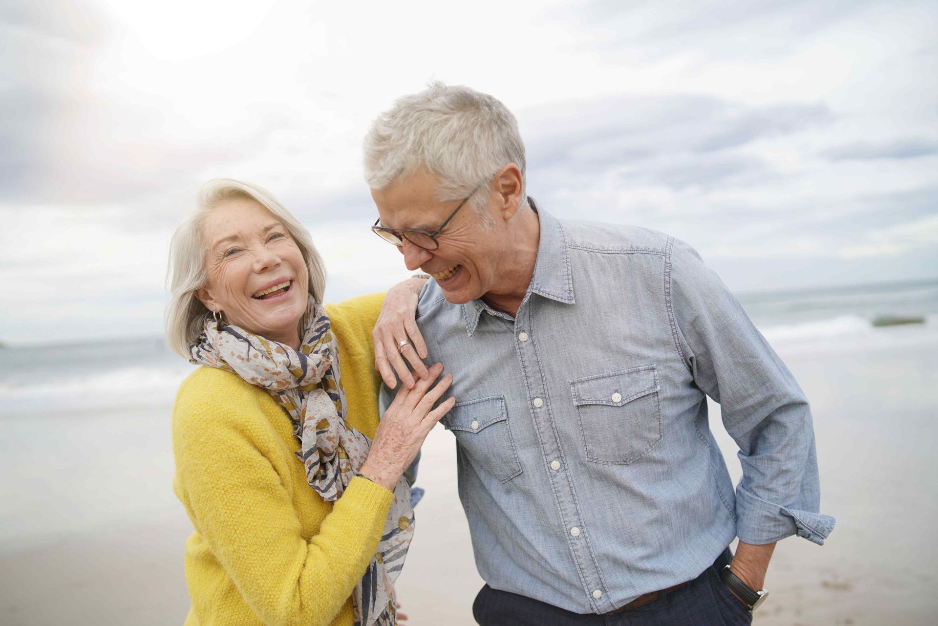 An elderly couple is standing next to each other on the beach.