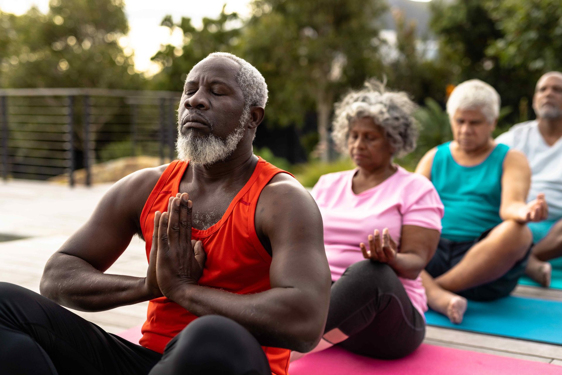 A group of older people are meditating on yoga mats outside.