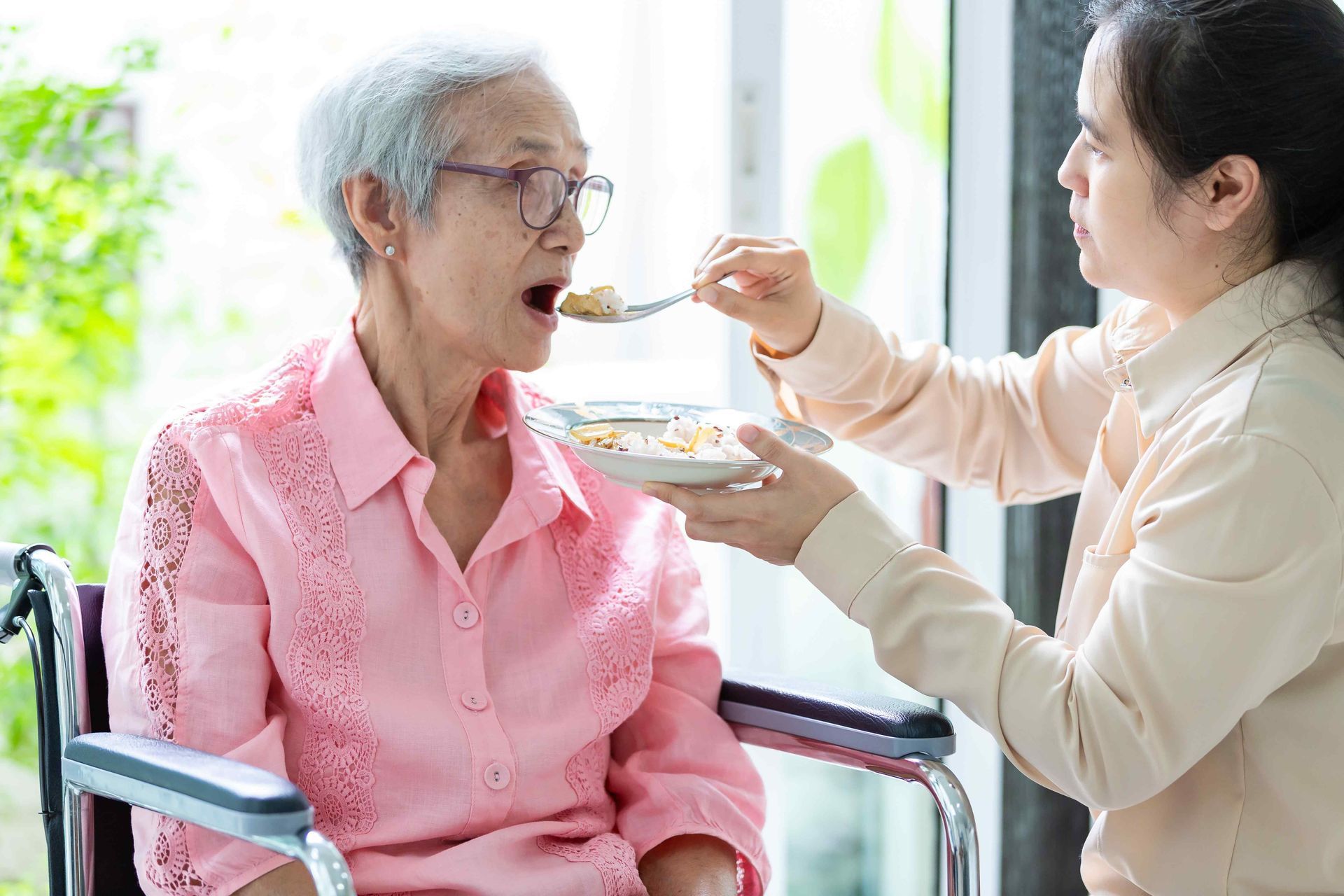 A woman is feeding an elderly woman in a wheelchair.