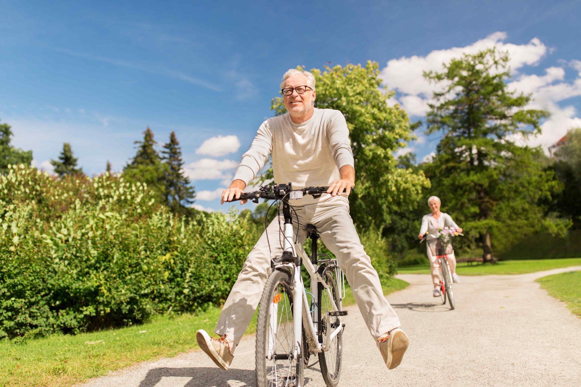 An elderly couple is riding bicycles down a path in a park.
