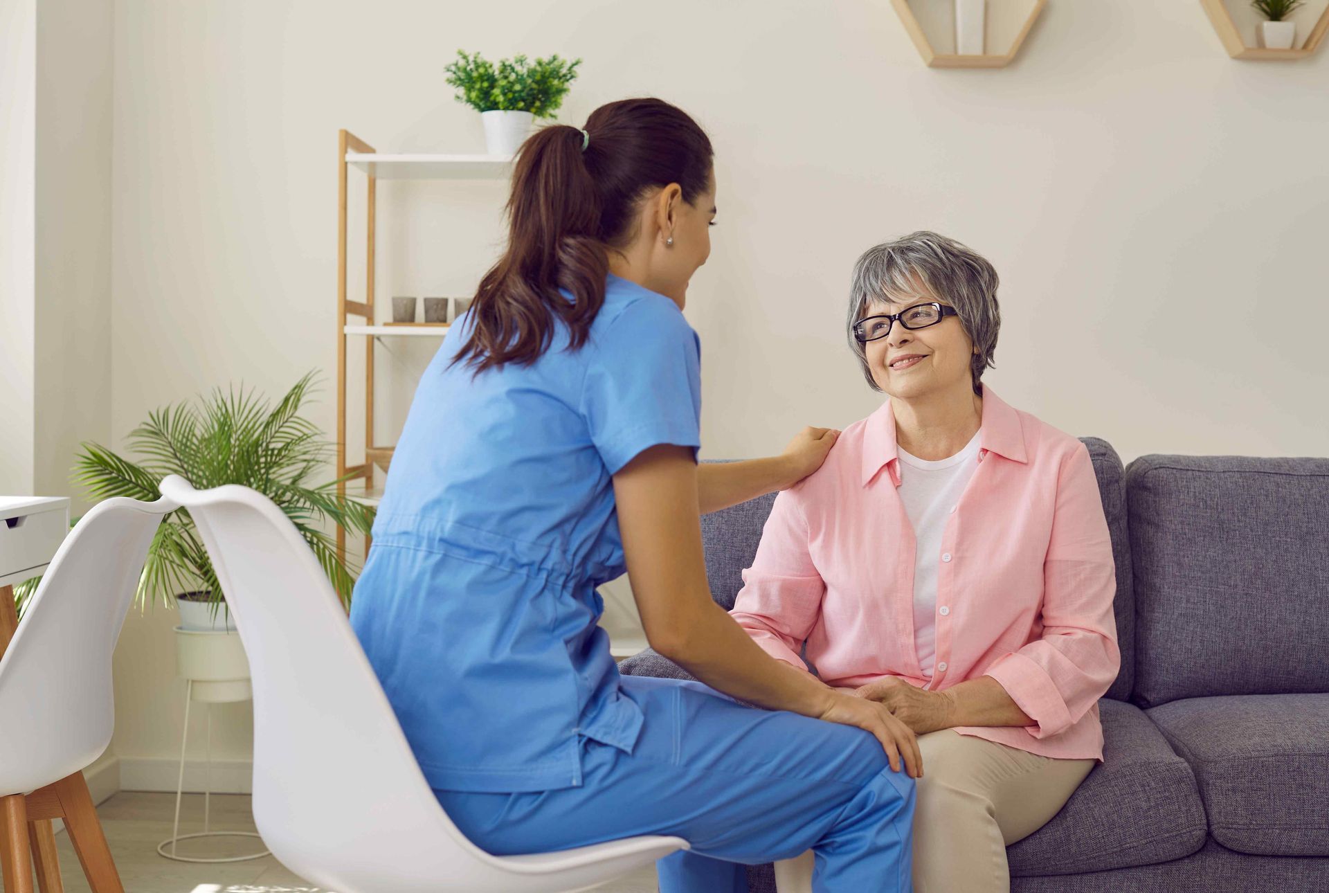 A nurse is sitting on a couch with an elderly woman.