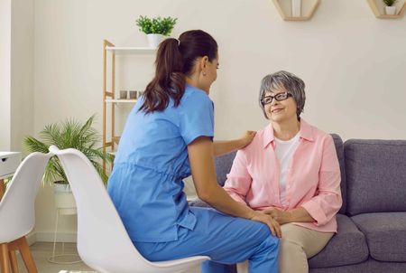 A nurse is sitting on a couch with an elderly woman.