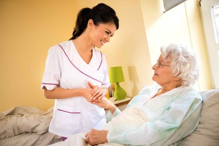 A nurse is talking to an elderly woman in a hospital bed.