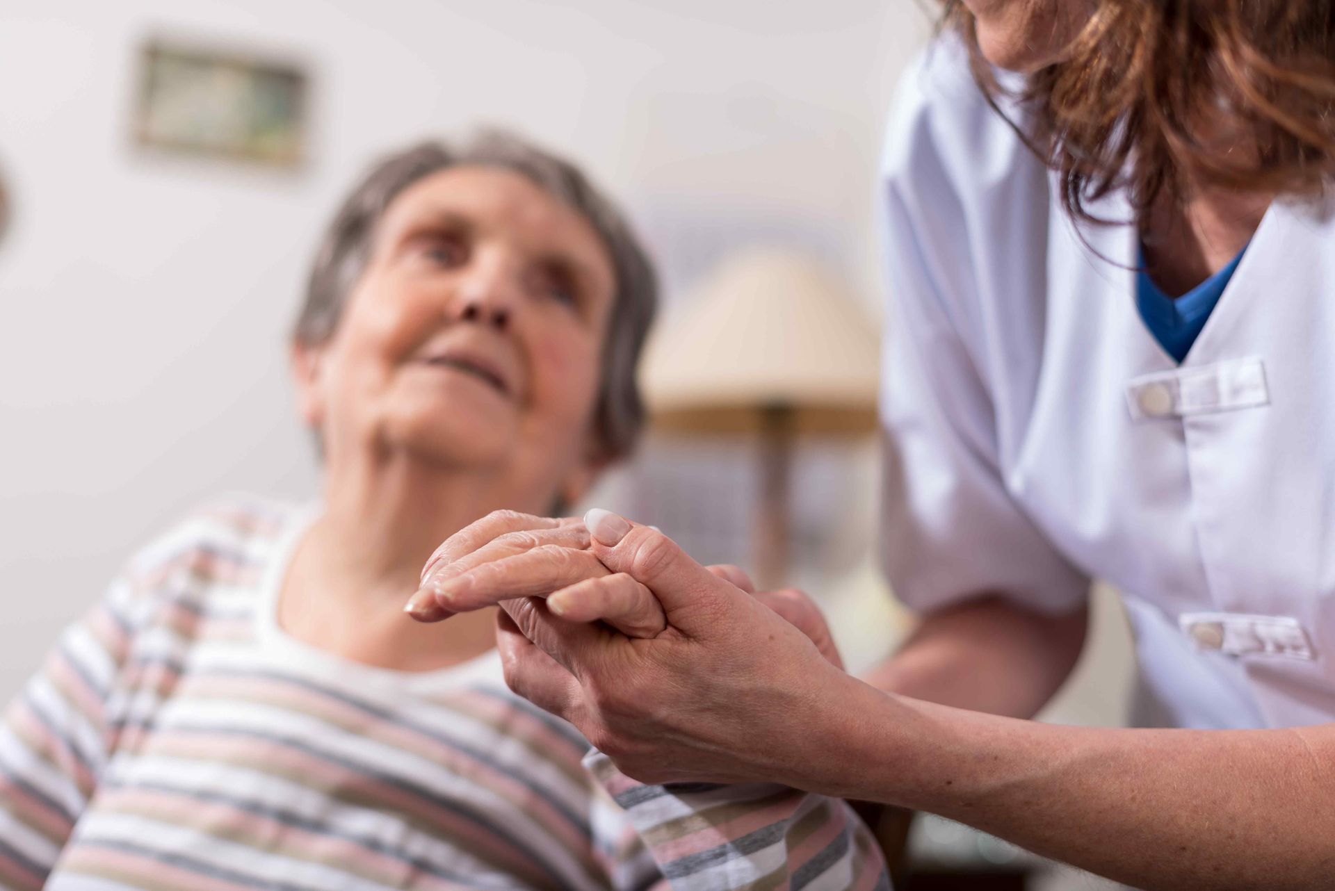 A nurse is holding the hand of an elderly woman.