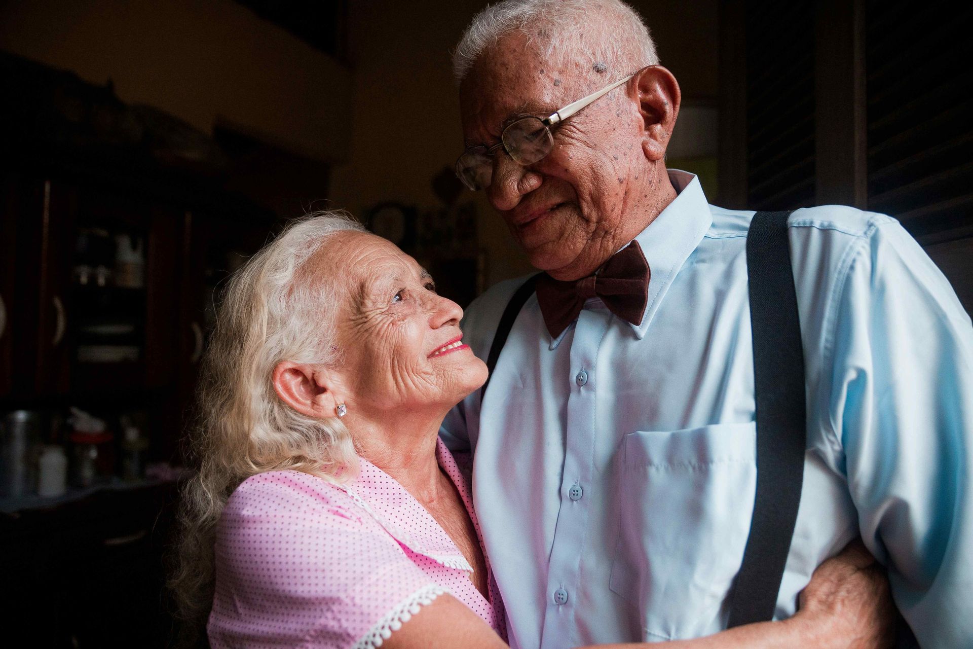 An elderly couple is dancing together in a living room.