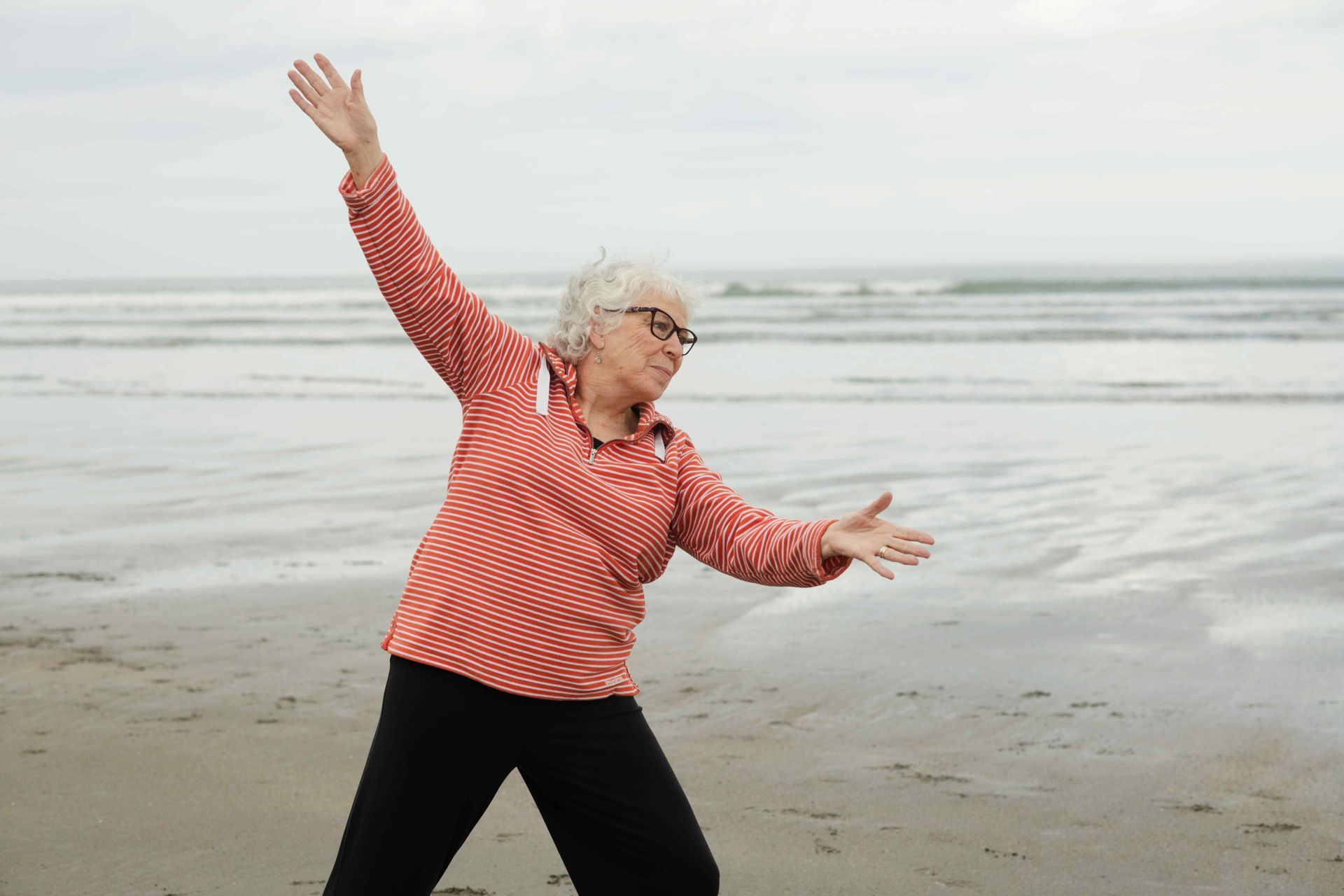 A woman is standing on a beach with her arms outstretched.