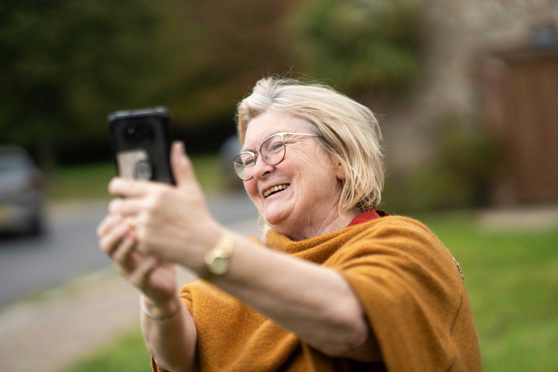An elderly woman is taking a selfie with her cell phone.