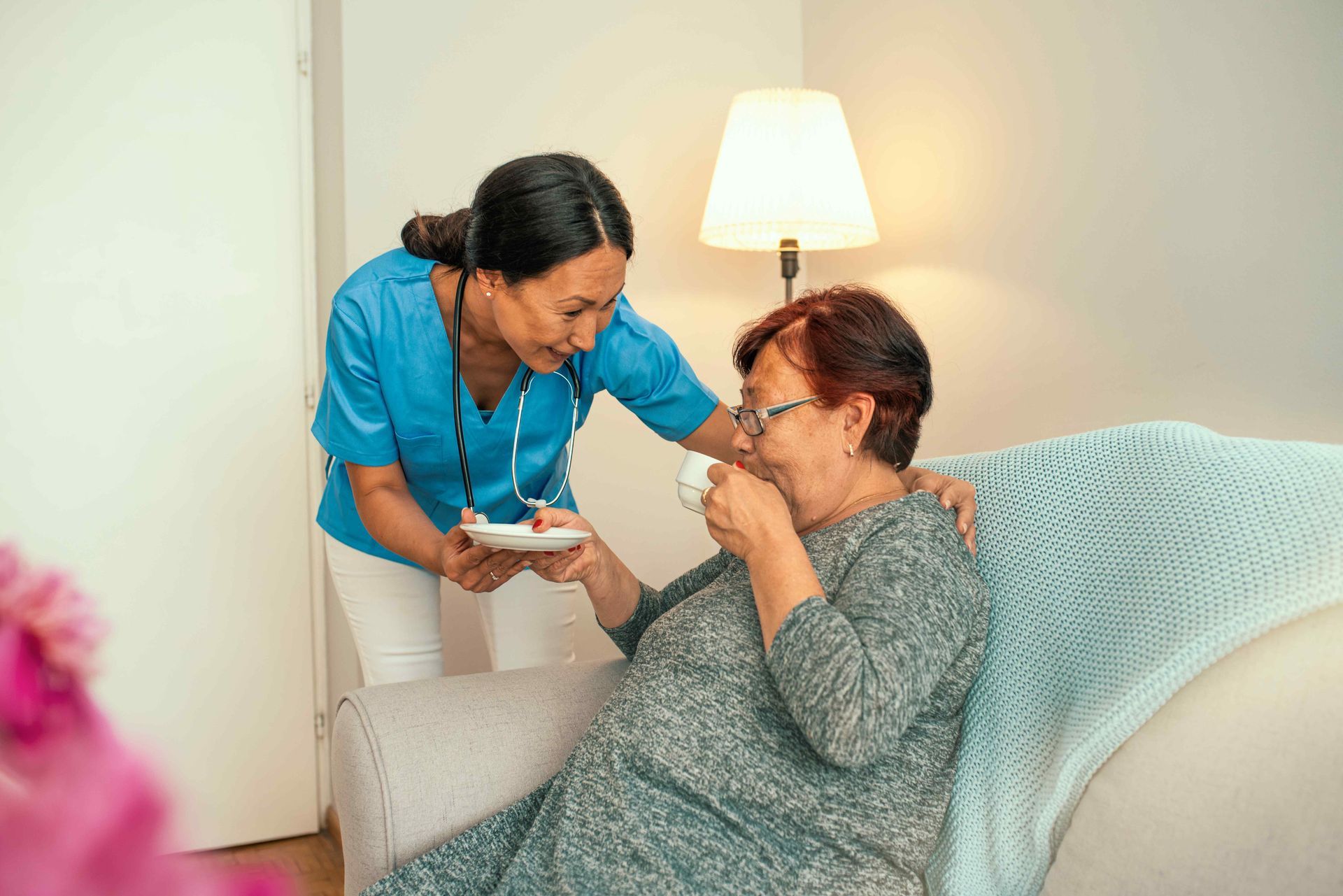 A nurse is giving an elderly woman a cup of coffee.